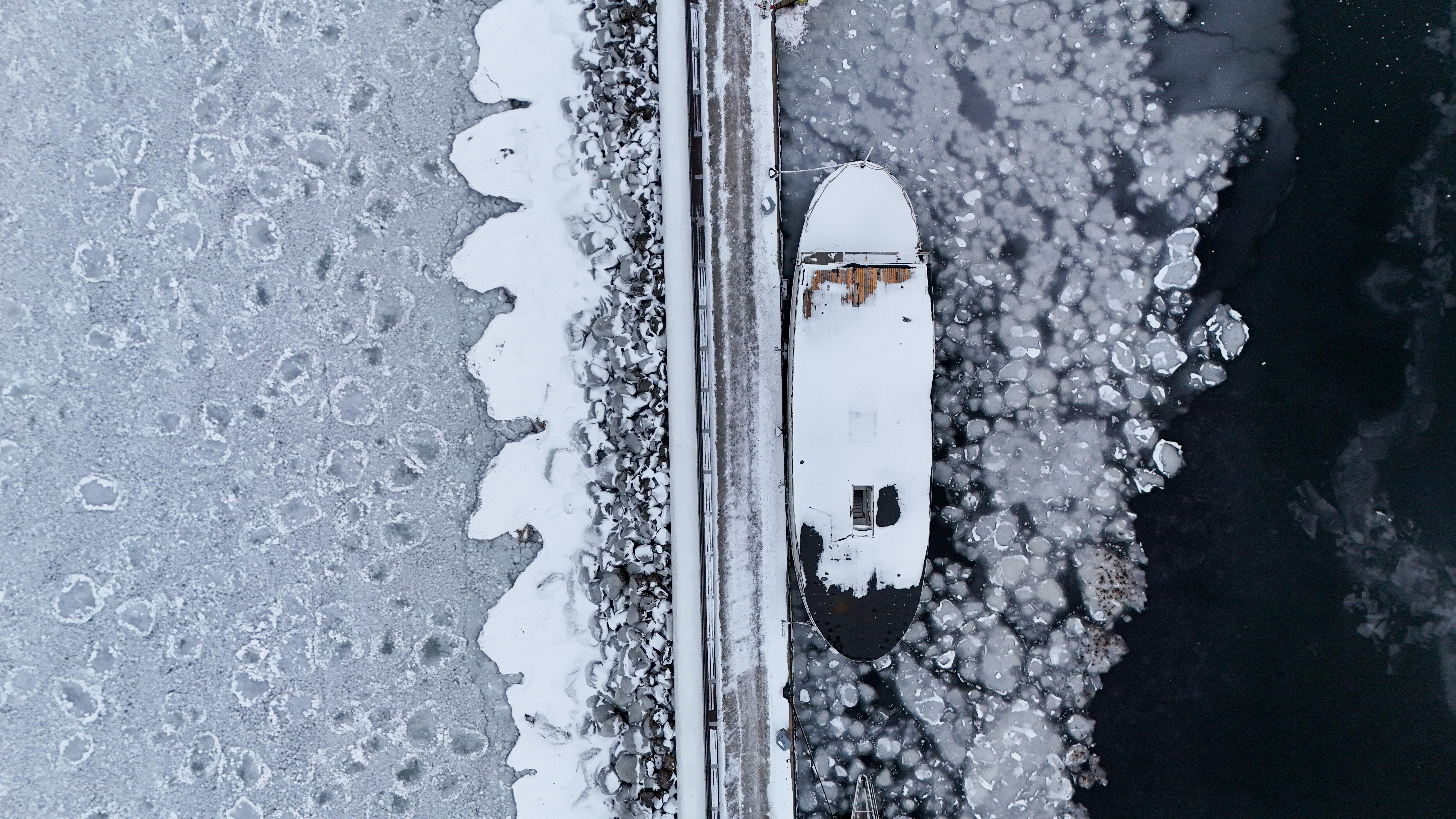 Kostenlos Luftaufnahme eines schneebedeckten Bootes, das im Winter in Jönköping, Schweden, an eisigen Gewässern vor Anker liegt. Stock-Foto