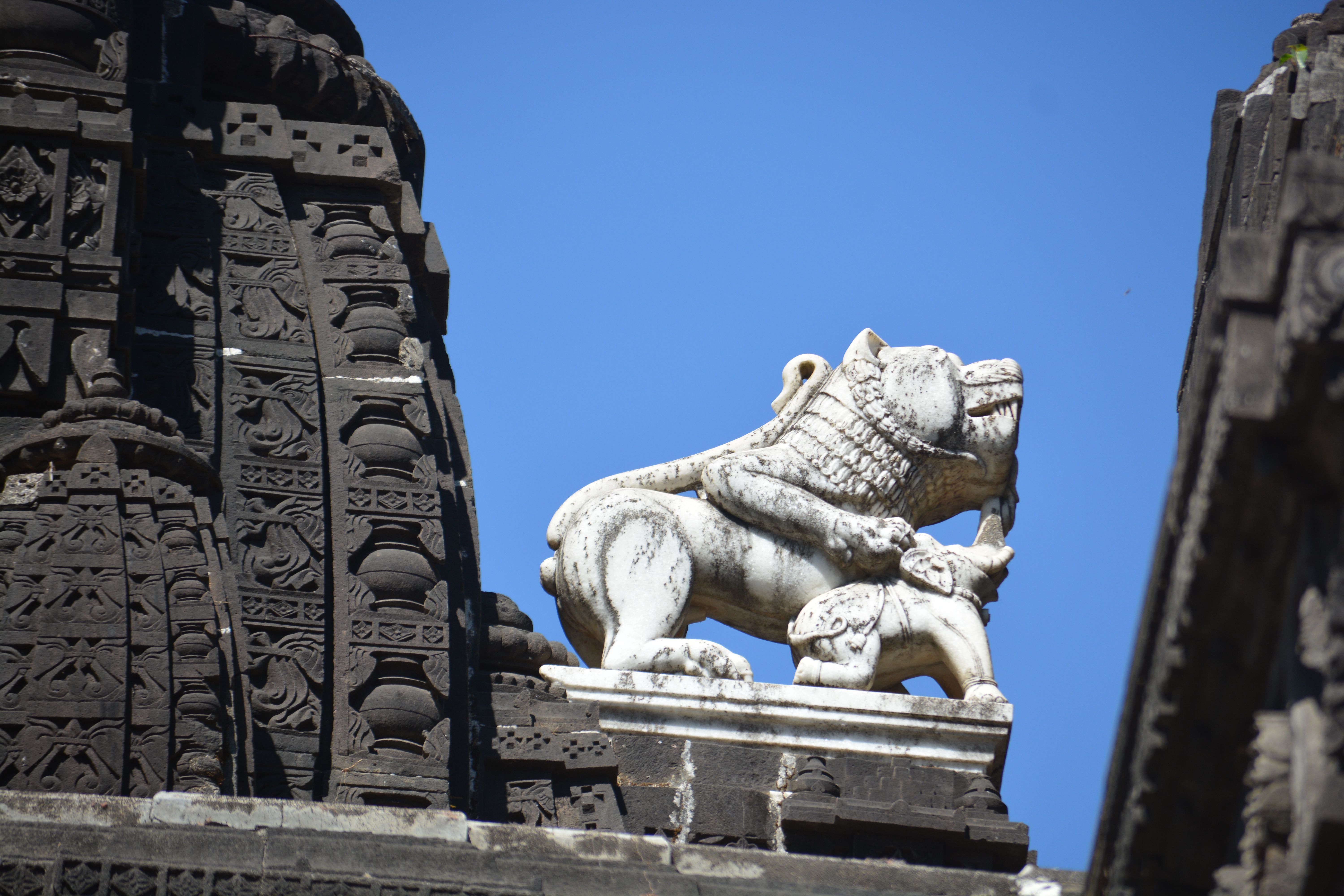 Close-up of a detailed temple sculpture featuring a lion figure against a clear blue sky.