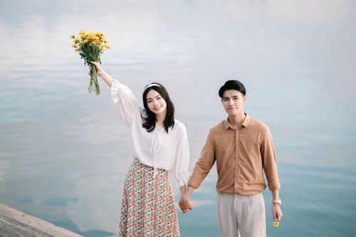 Free Happy couple holding hands by the lake, woman with yellow flowers. Stock Photo