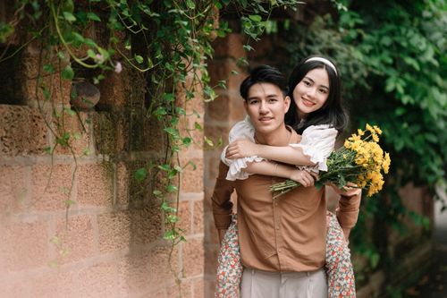 Free A happy young couple with flowers, enjoying a romantic moment outdoors by a brick wall. Stock Photo