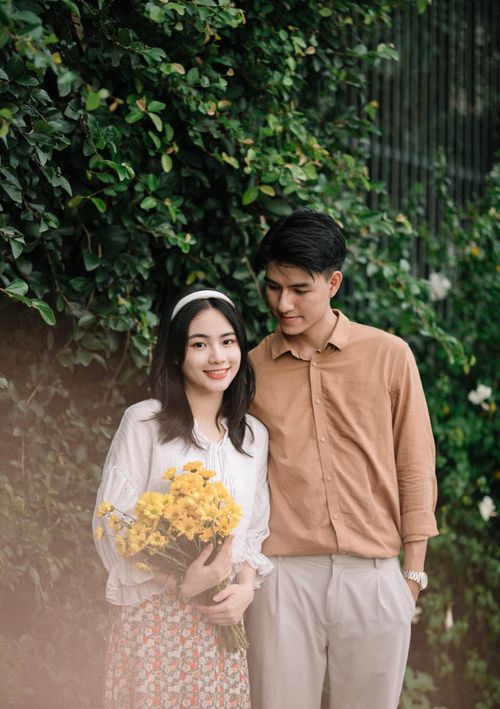 Free Charming couple enjoying a moment outdoors, surrounded by lush greenery and holding yellow flowers. Stock Photo