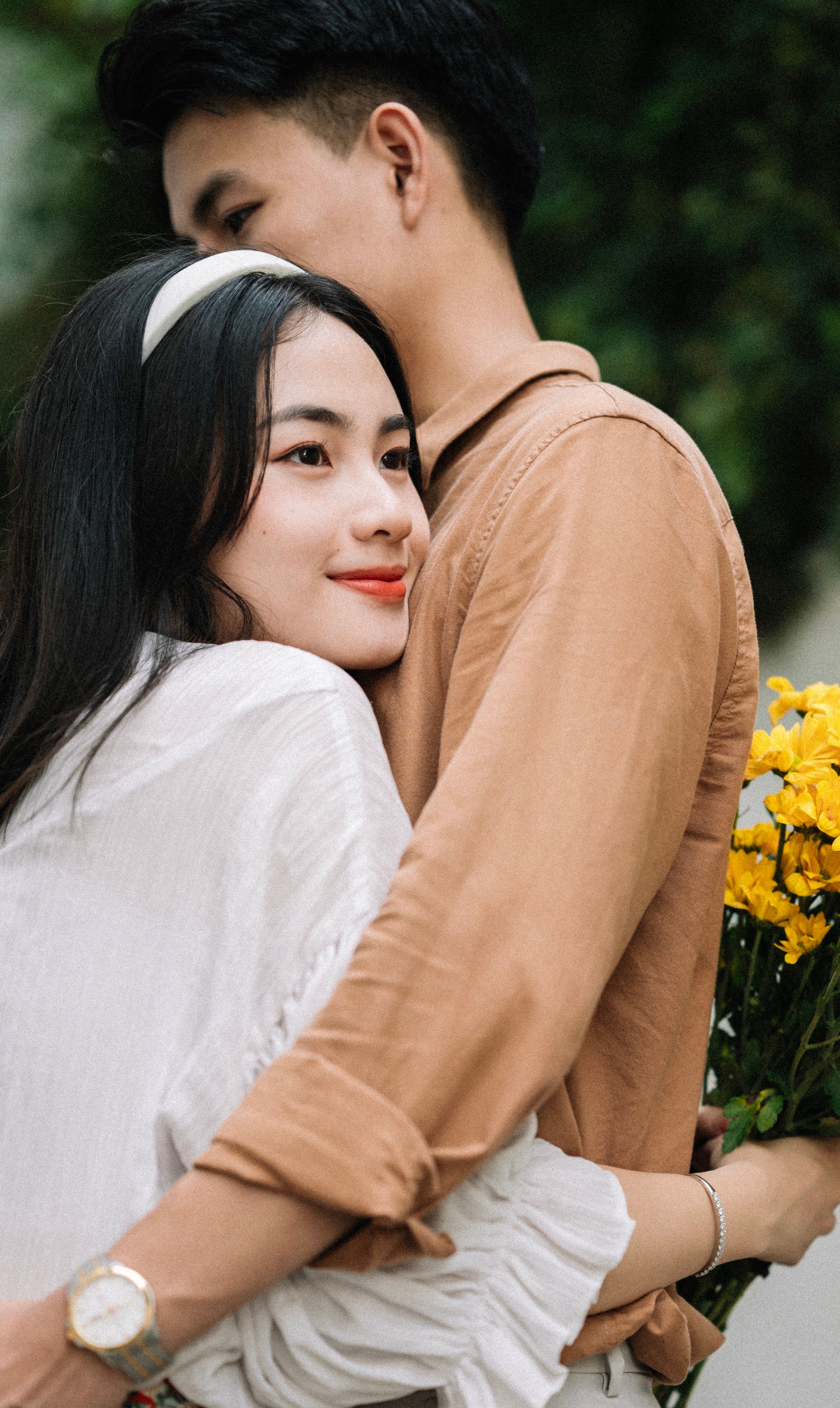 A young couple sharing an affectionate embrace outdoors, holding yellow flowers.