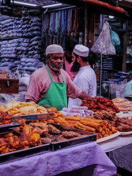 A street vendor in a vibrant market setting selling diverse fried foods.