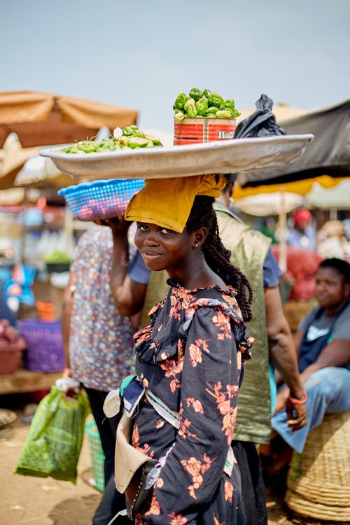 Free A woman carries produce on her head at a bustling market in Accra, Ghana, outdoors. Stock Photo