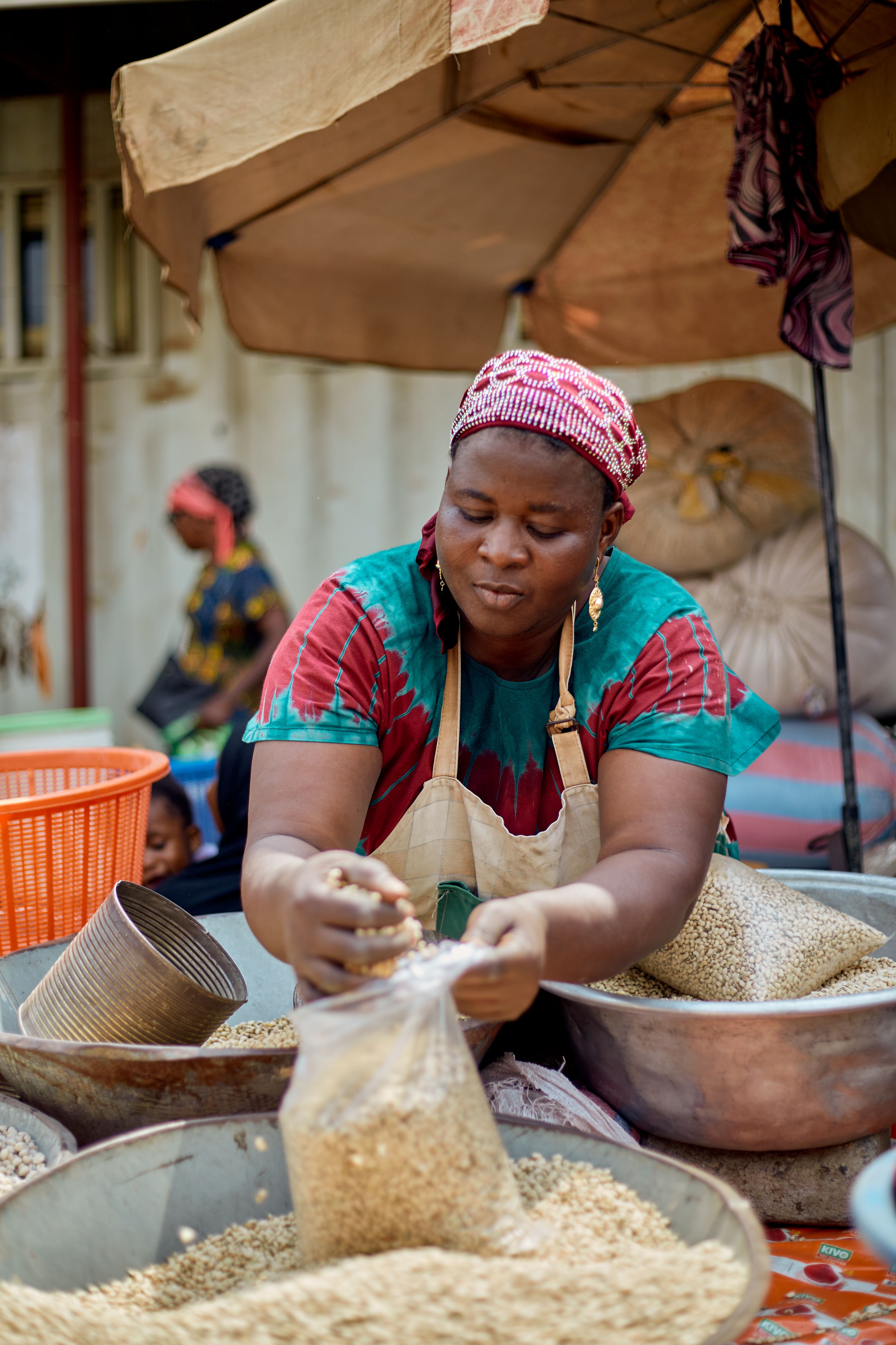 African woman in a vibrant market setting packaging grains in a bag. Captured in Accra, Ghana.