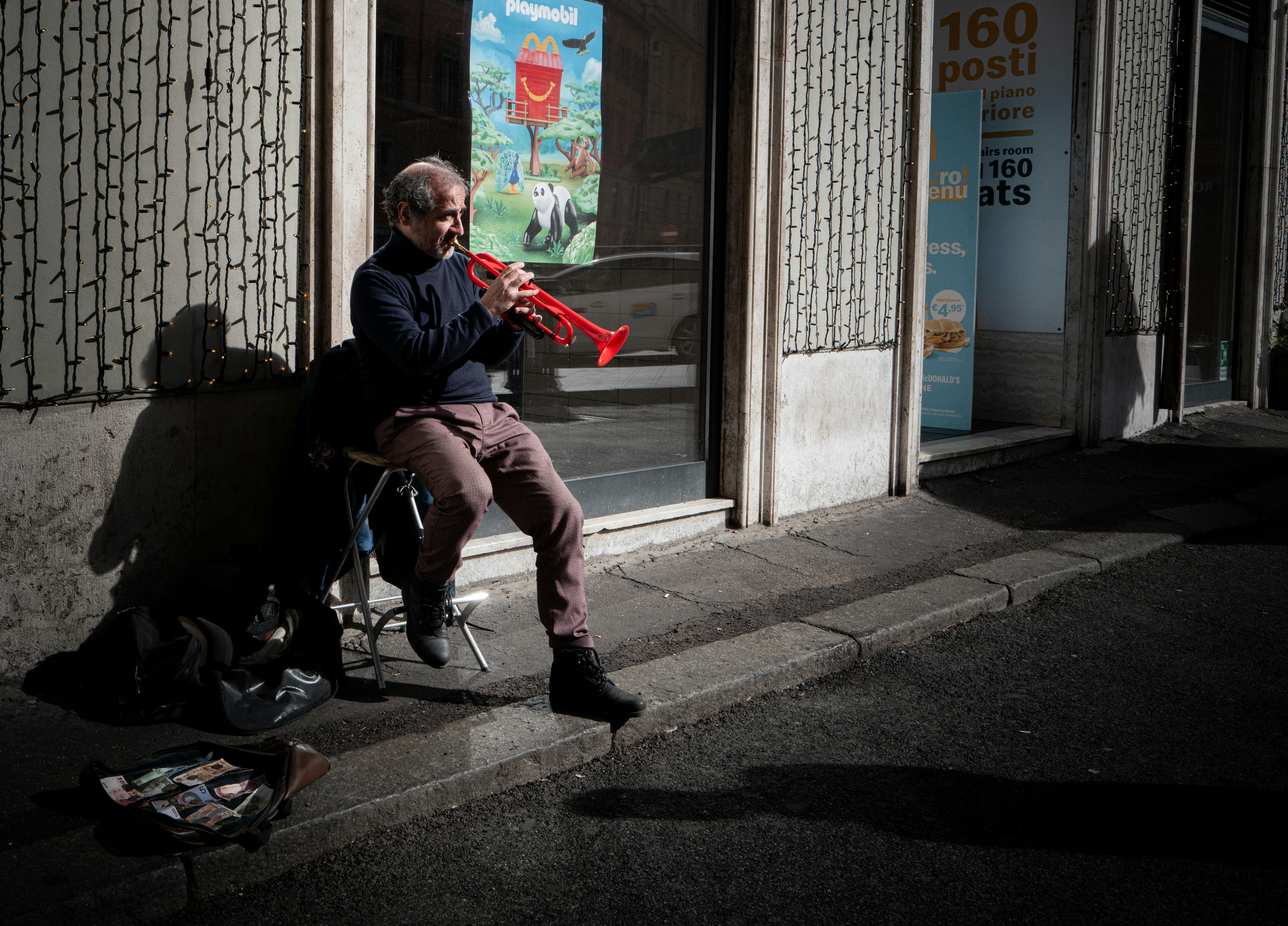 Ücretsiz İtalya'nın Roma kentinde, yaşlı bir sokak müzisyeni parlak kırmızı bir trompet çalarak kentsel kültürü yansıtıyor. Stok Fotoğraflar