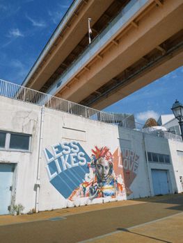 Colorful street art with message 'Less Likes More Love' under bridge in Kobe, Japan.