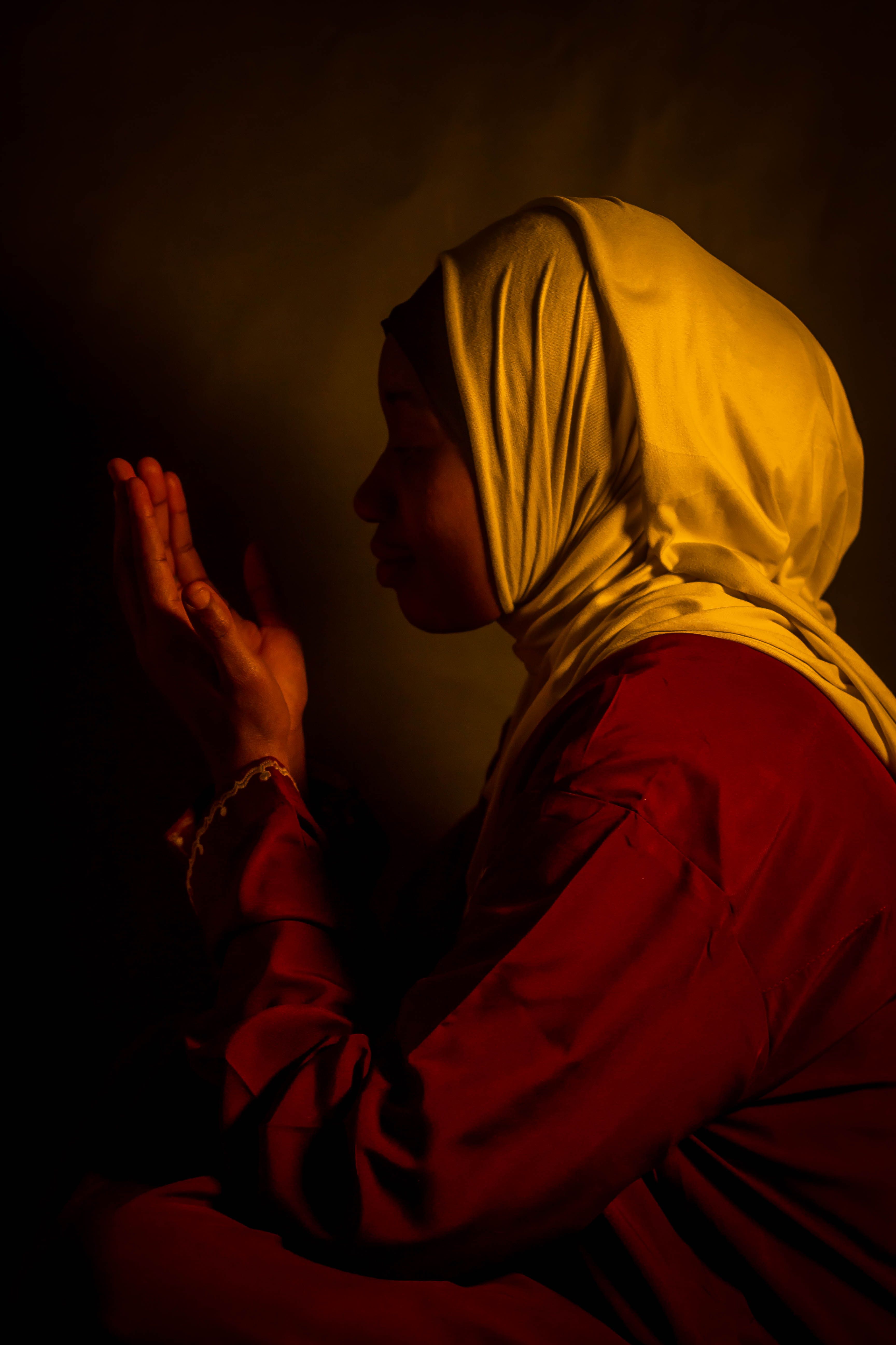 Silhouette of a woman in a hijab silently praying, captured in warm lighting.