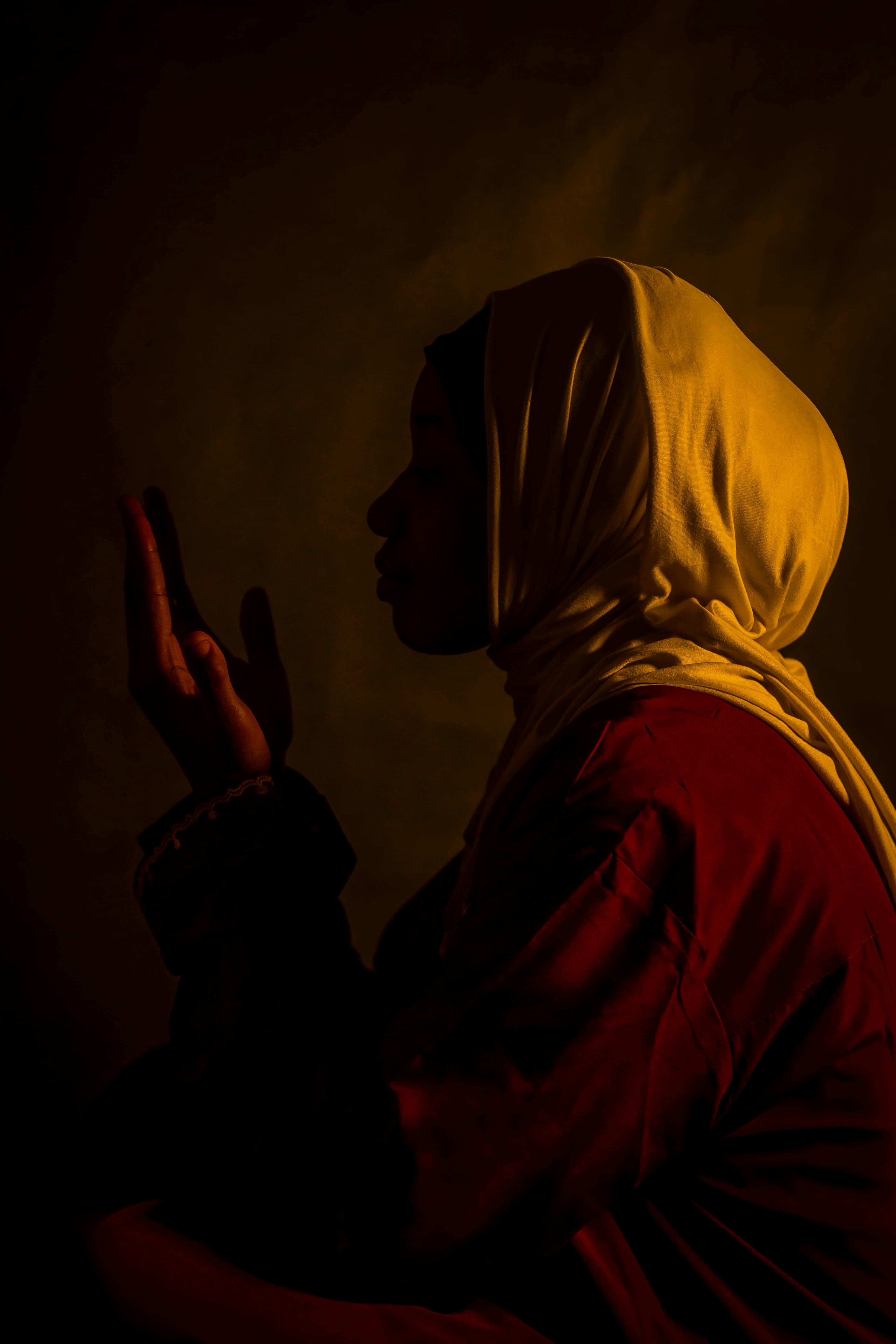 Ücretsiz Sıcak ve loş bir ışık altında dua eden başörtülü bir kadının silueti, dramatik ve huzurlu bir atmosfer yaratıyor. Stok Fotoğraflar