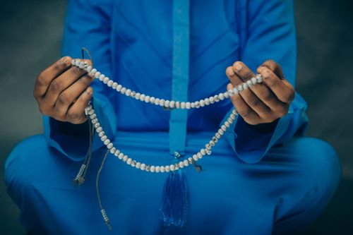Free A person in blue clothing holds prayer beads in their hands, symbolizing meditation or religious practice. Stock Photo