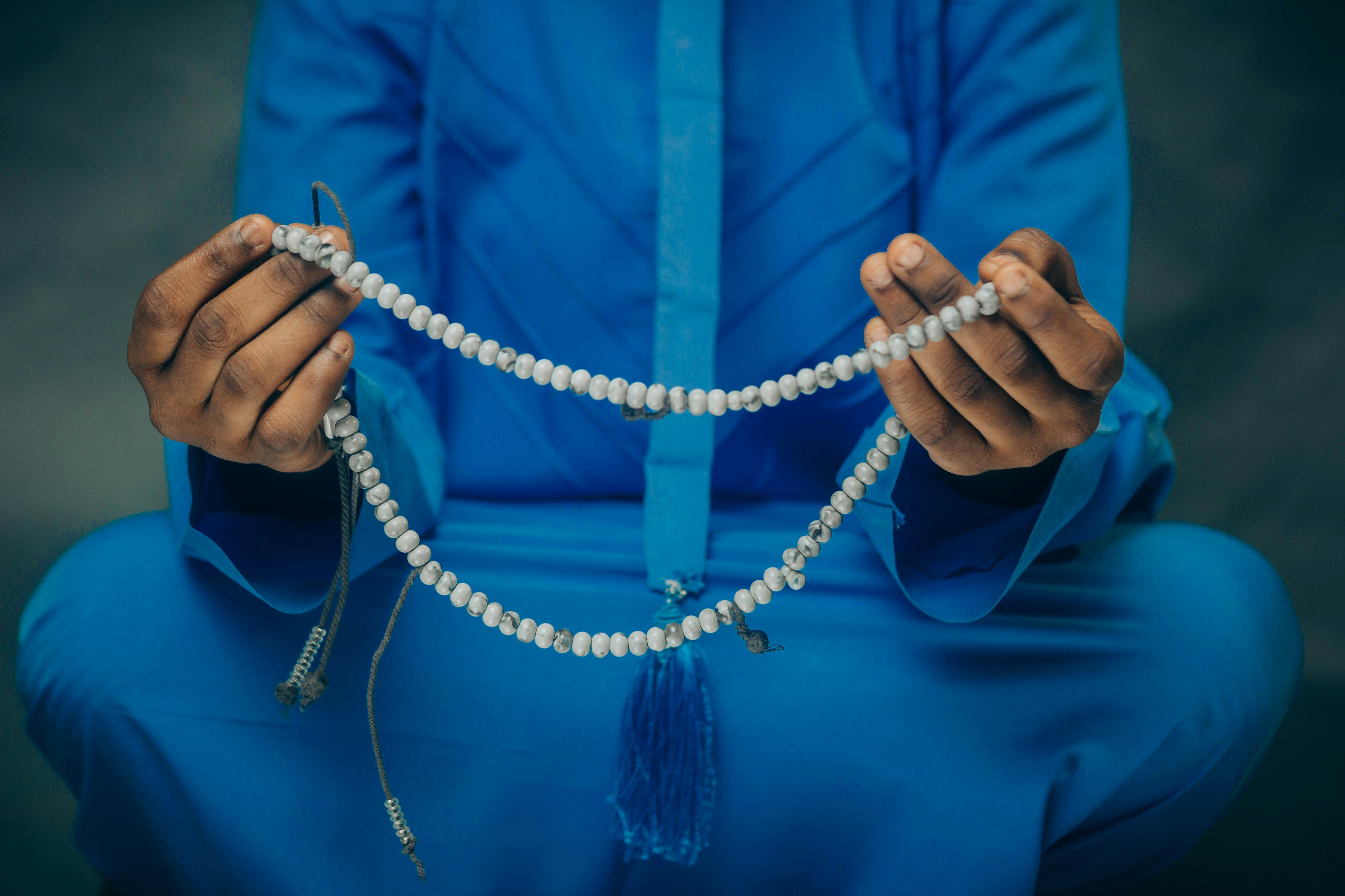 Ücretsiz Mavi giysili bir kişi ellerinde tesbih tutuyor; bu, meditasyonu veya dini uygulamayı simgeliyor. Stok Fotoğraflar