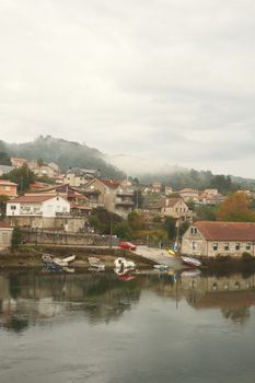 Scenic view of a misty Galician town reflecting on water with rustic charm.