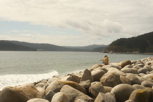 Free A lone traveler rests on rocky coast in Galicia, Spain's serene seaside. Stock Photo
