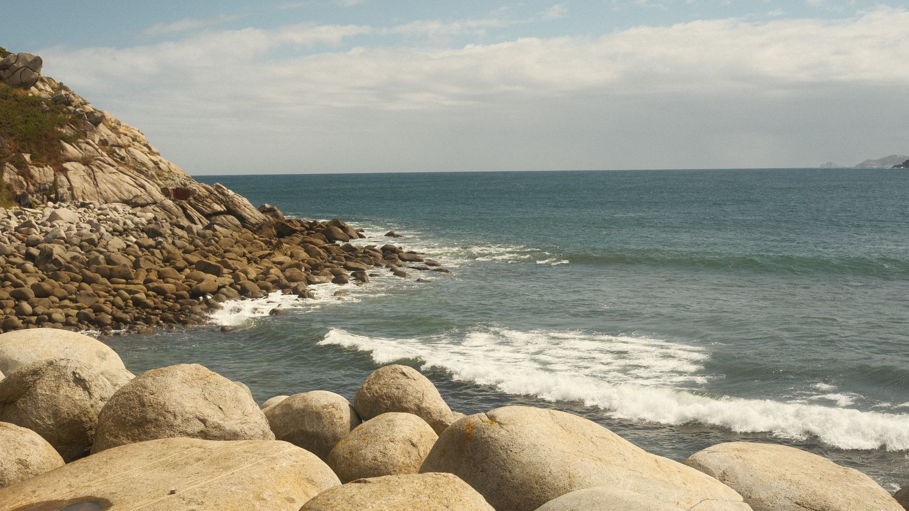 Serene view of rocky coastline in Galicia, Spain with gentle ocean waves and clear skies.