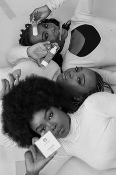 Black and white portrait of three women holding skincare and beauty products in a graceful pose.