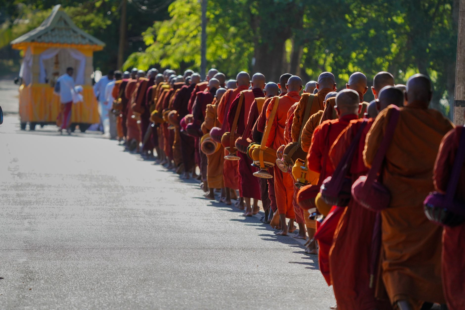 A line of Buddhist monks in orange robes walk in a spiritual procession in Sri Lanka on a sunny day.