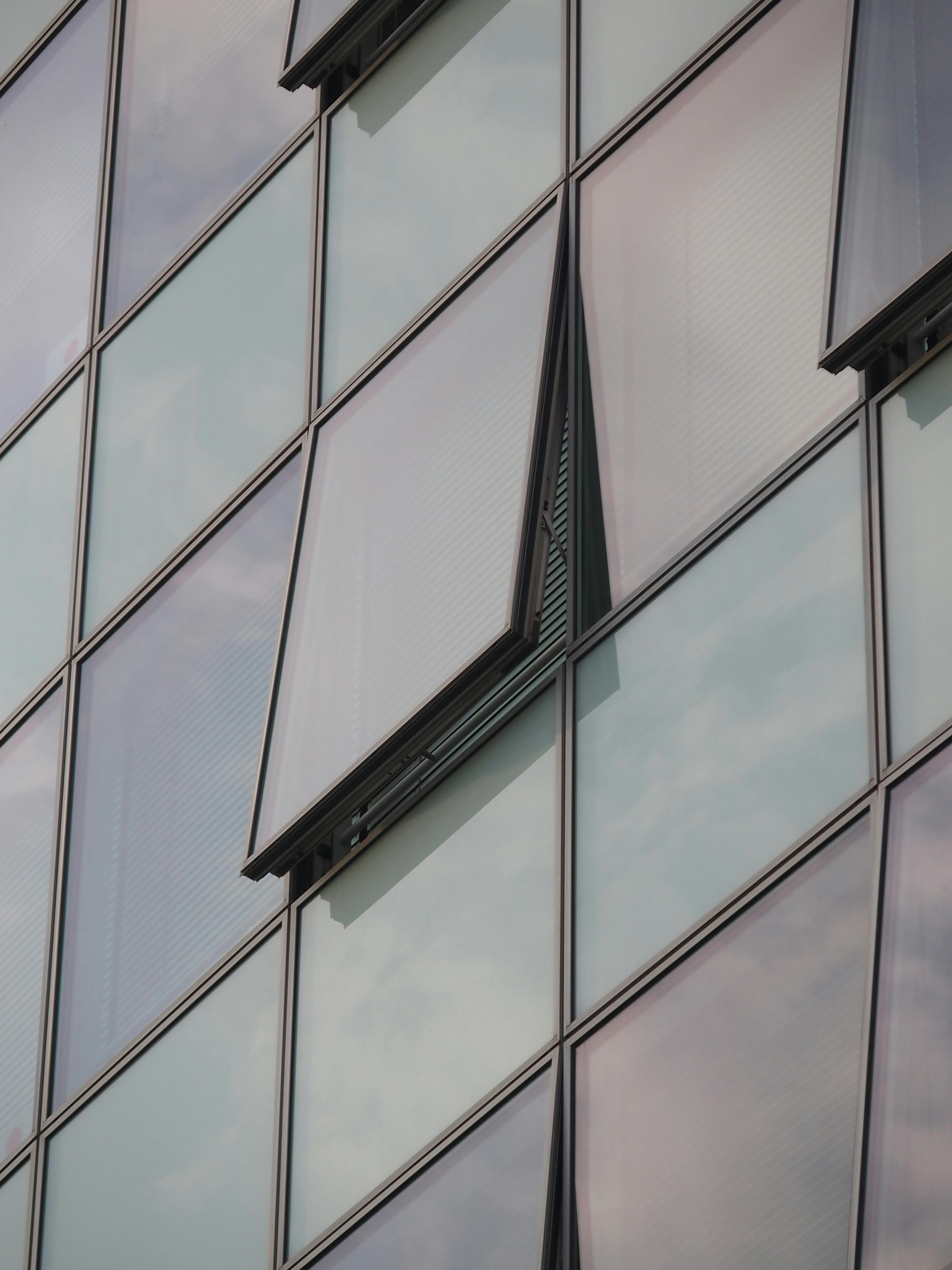 Kostenlos Nahaufnahme einer modernen Glasfassade mit offenen Fenstern, die den Himmel spiegelt. Stock-Foto