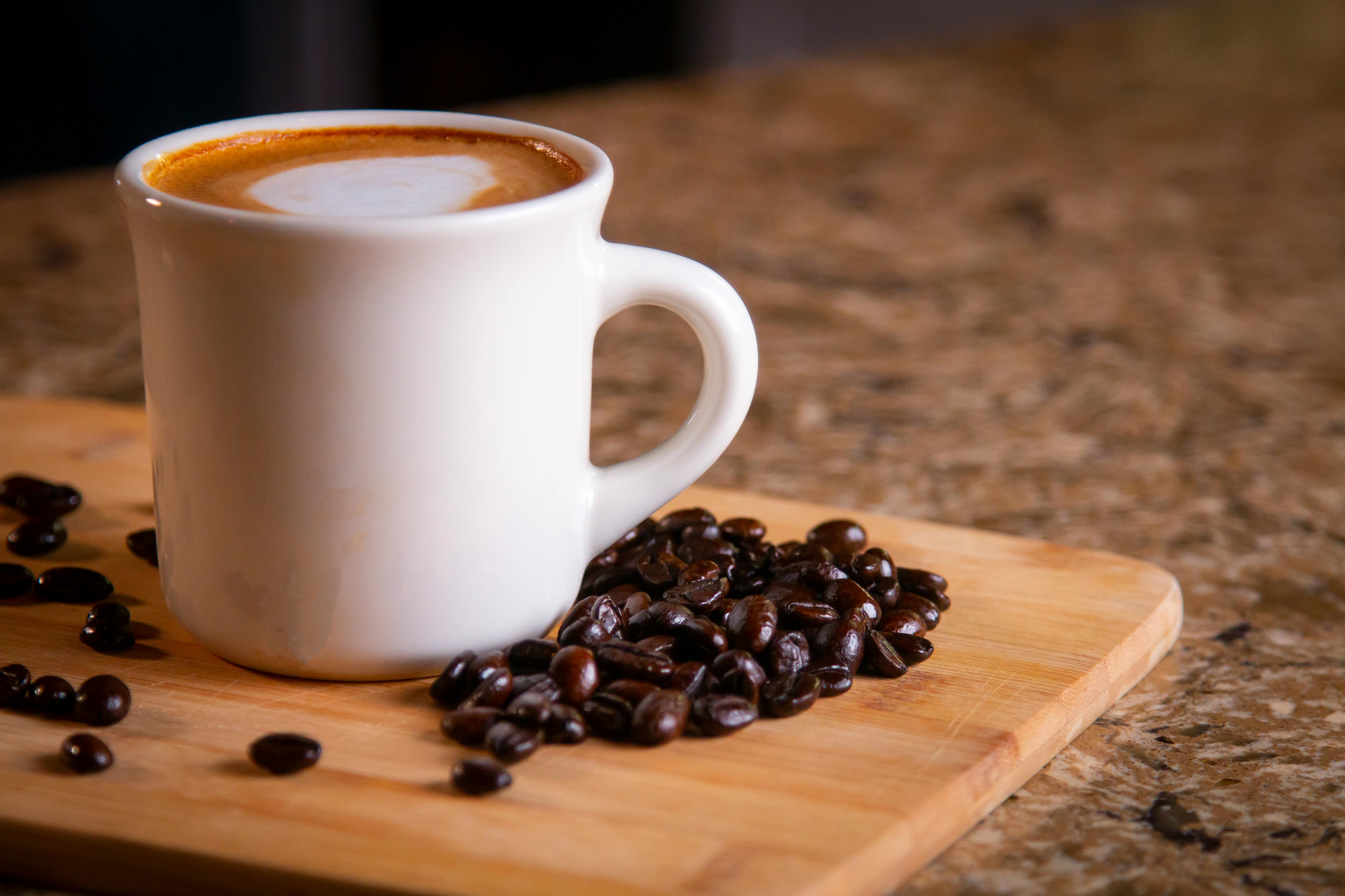 A close-up of a steaming cup of coffee with scattered roasted coffee beans on a wooden board.