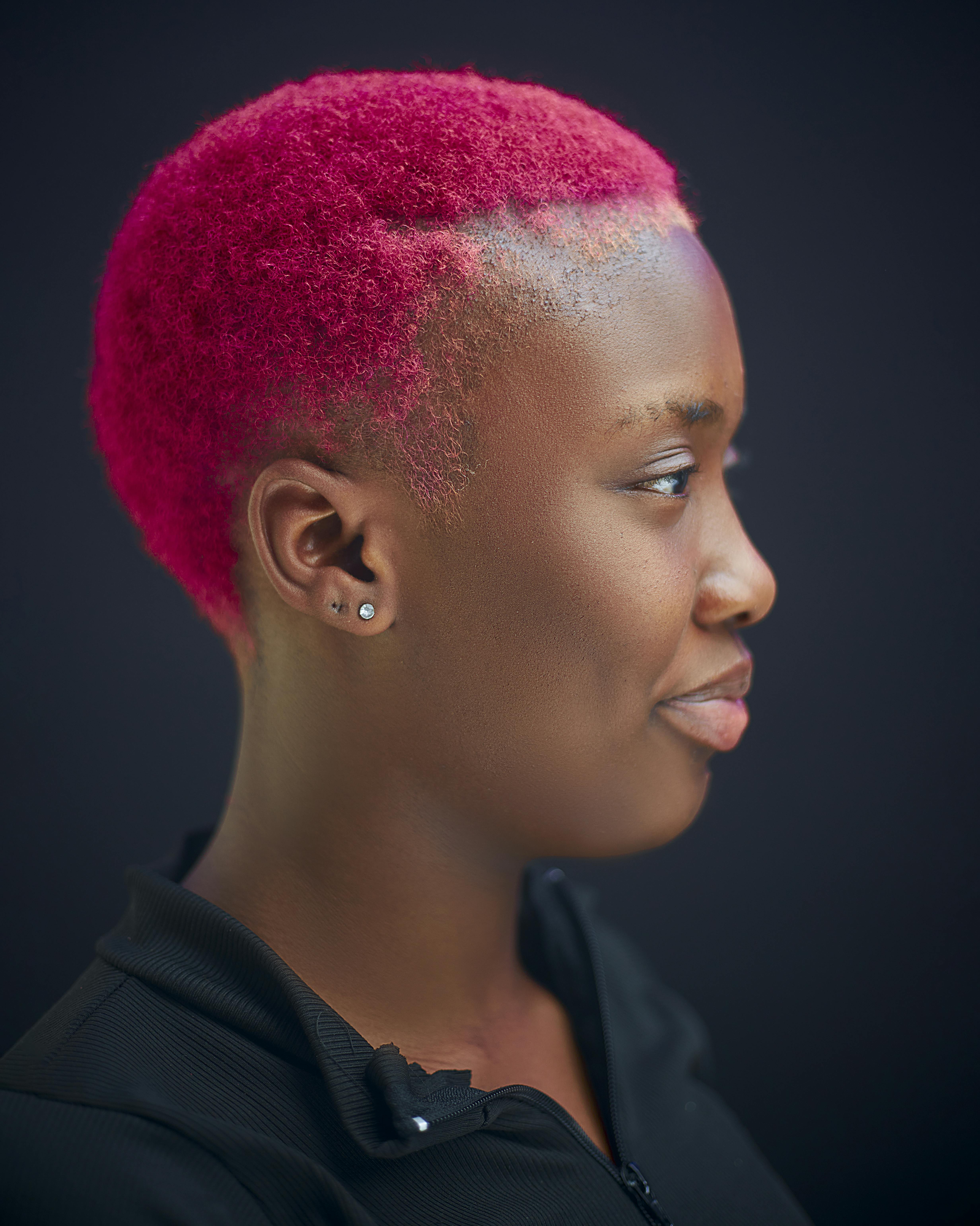 Profile portrait of a woman with vibrant pink hair on a dark background.