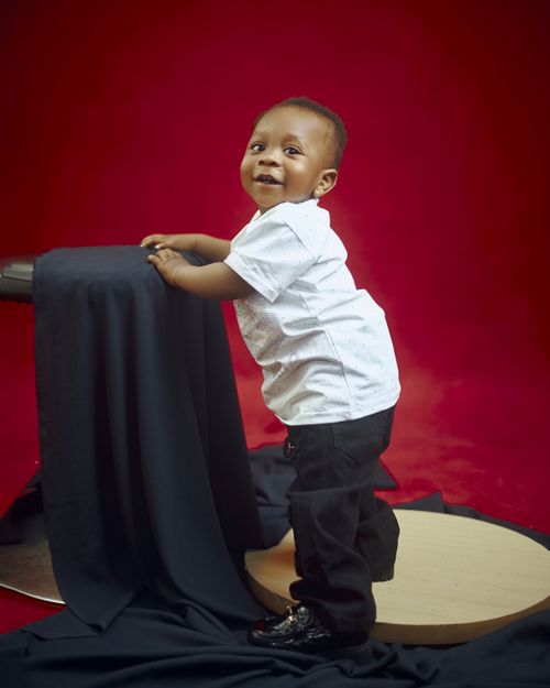 Free Cute baby in stylish outfit posing on red background with black drapery. Stock Photo