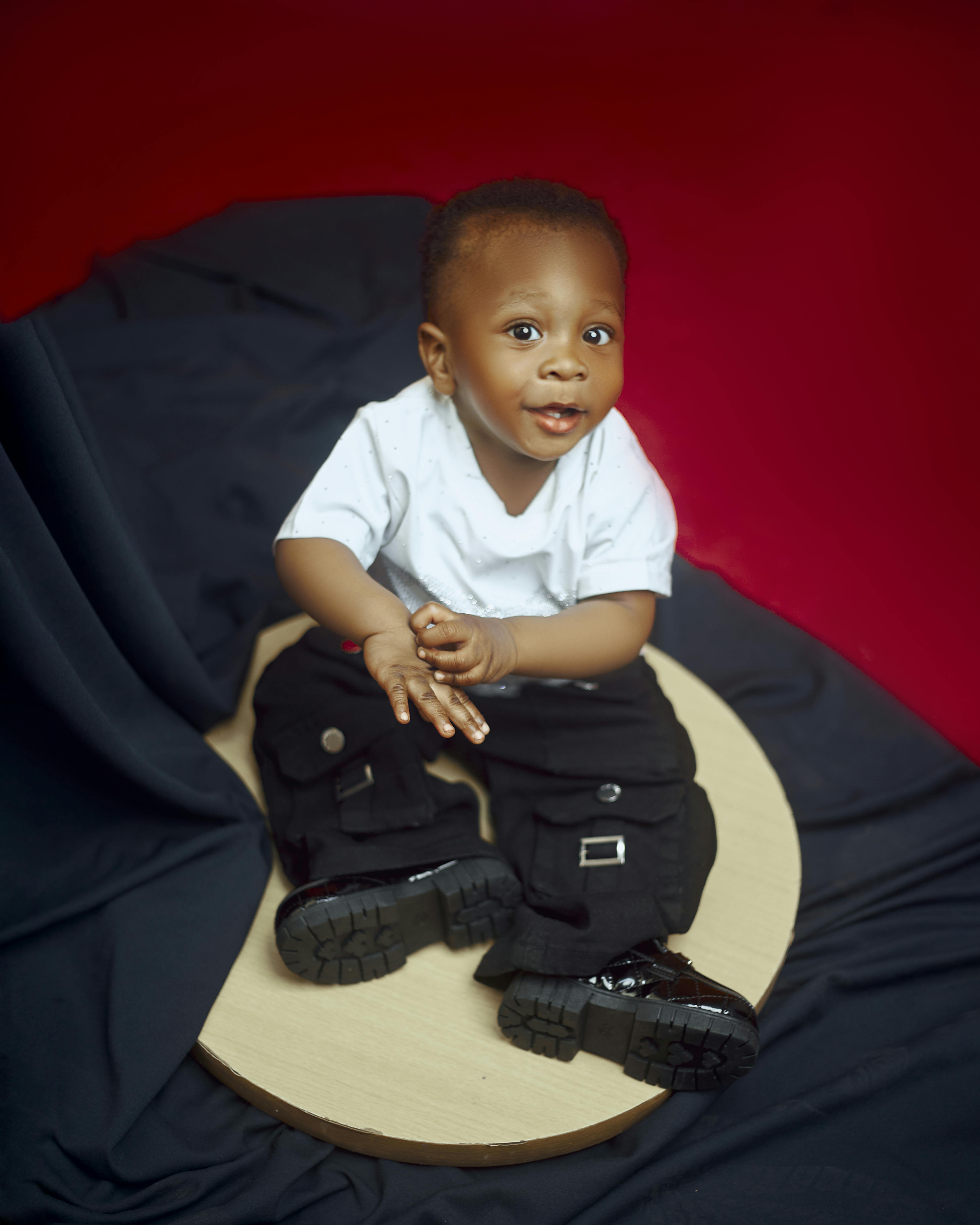 Kostenlos Ein süßes Baby in einem schicken Outfit sitzt vor einem Stoffhintergrund und lächelt in die Kamera. Stock-Foto