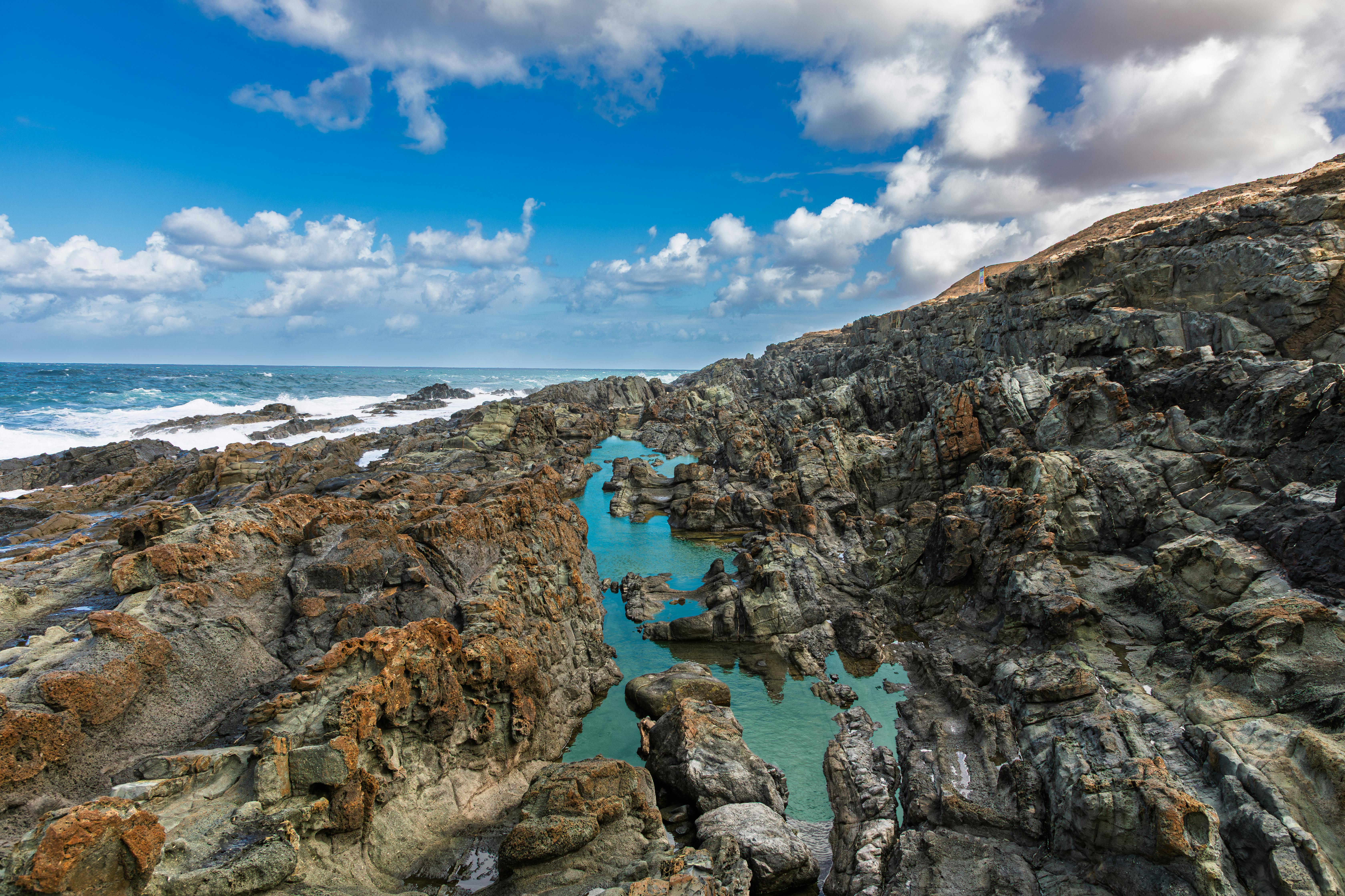 Stunning view of the rugged coastline in Lanzarote, showcasing volcanic rock formations and blue waters under a bright sky.