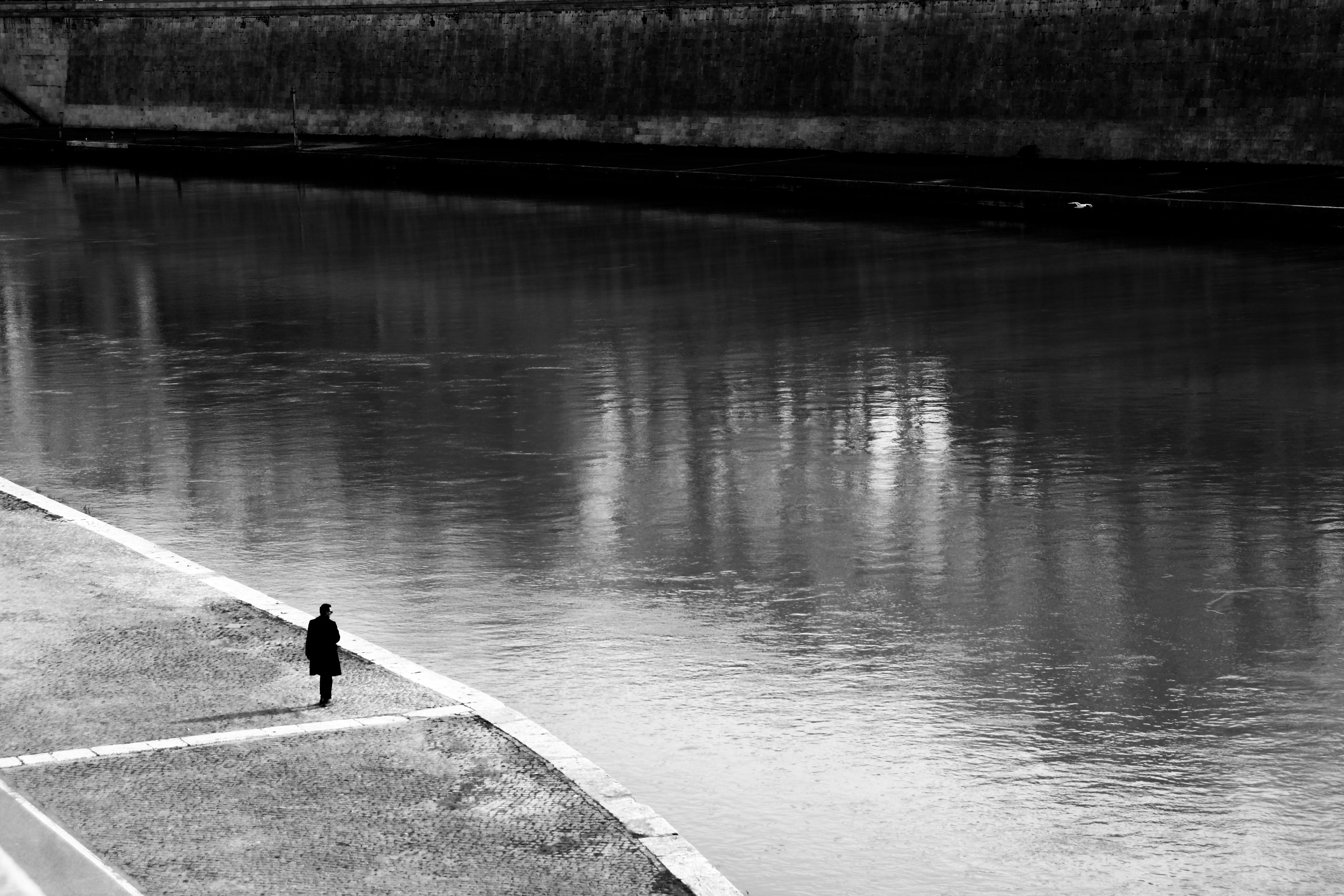 Ücretsiz Roma'da Tiber Nehri kıyısında yalnız bir figür yürüyor; bu görüntü, yalnızlığı ve tefekkürü çağrıştırıyor. Stok Fotoğraflar