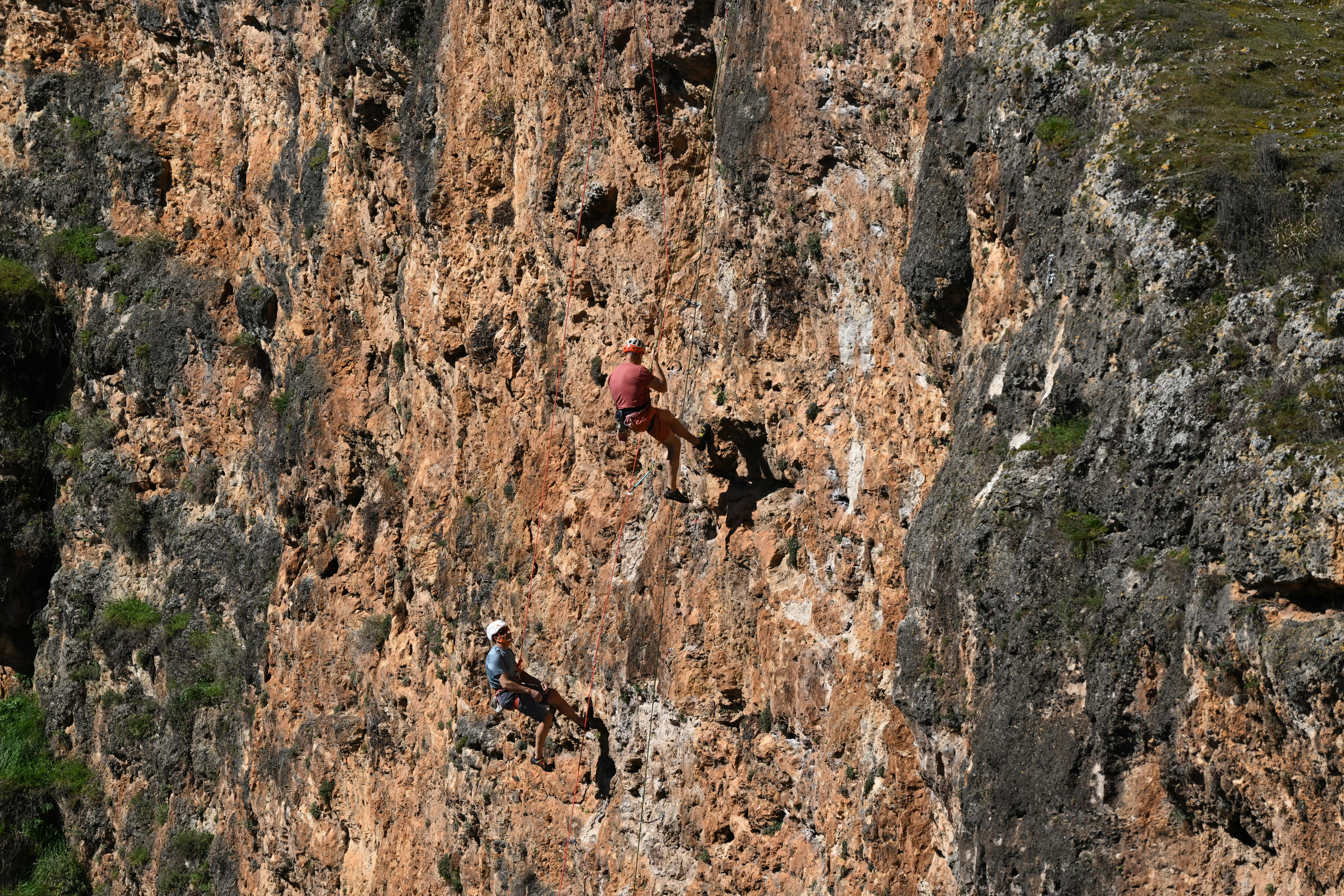 Безкоштовне Двоє альпіністів піднімаються на крутий скелястий обрив за яскравого денного світла, демонструючи пригоди та майстерність. стокове фото
