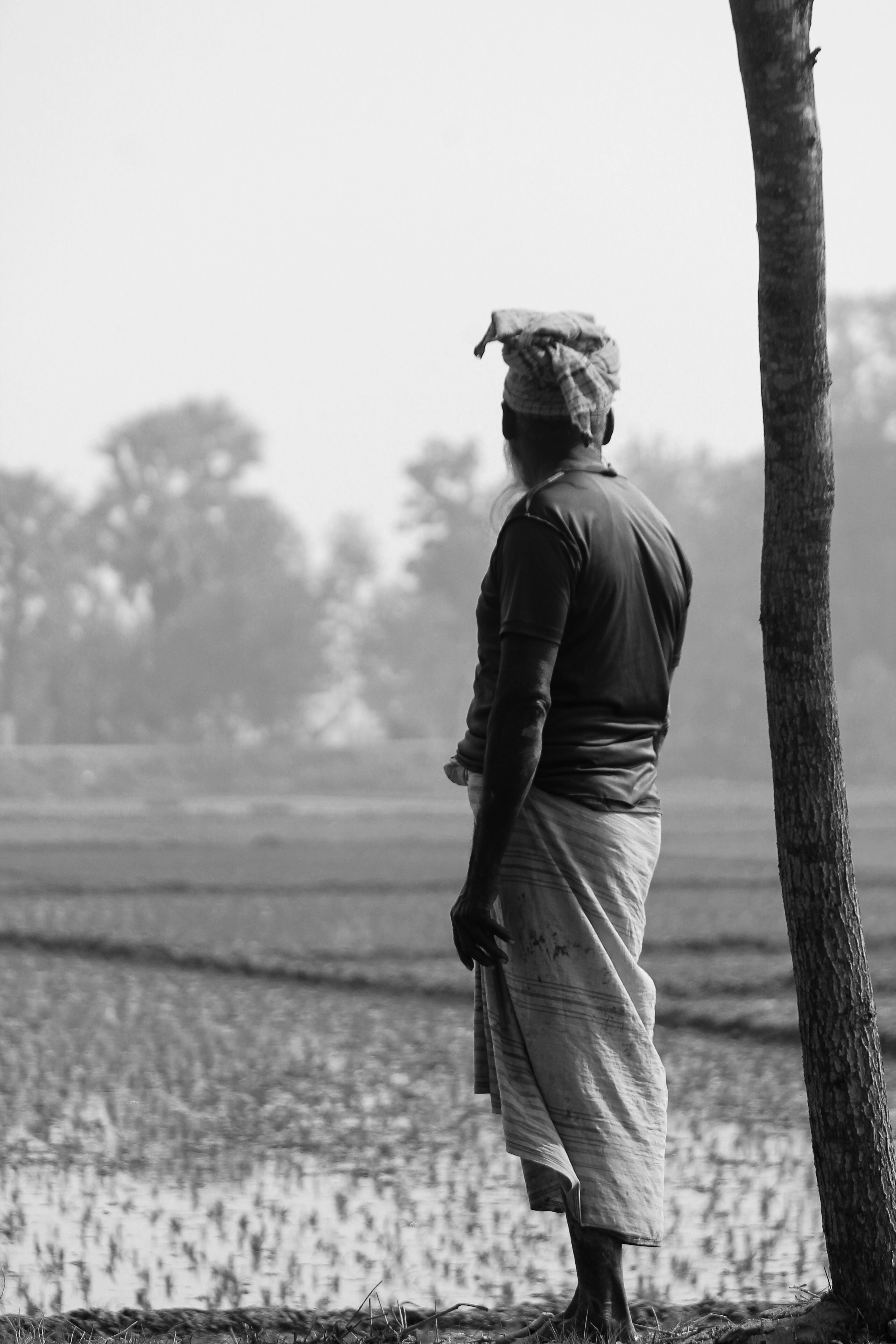 Gratis Immagine in bianco e nero di un contadino in abiti tradizionali, in piedi pensieroso in un campo tranquillo. Foto a disposizione