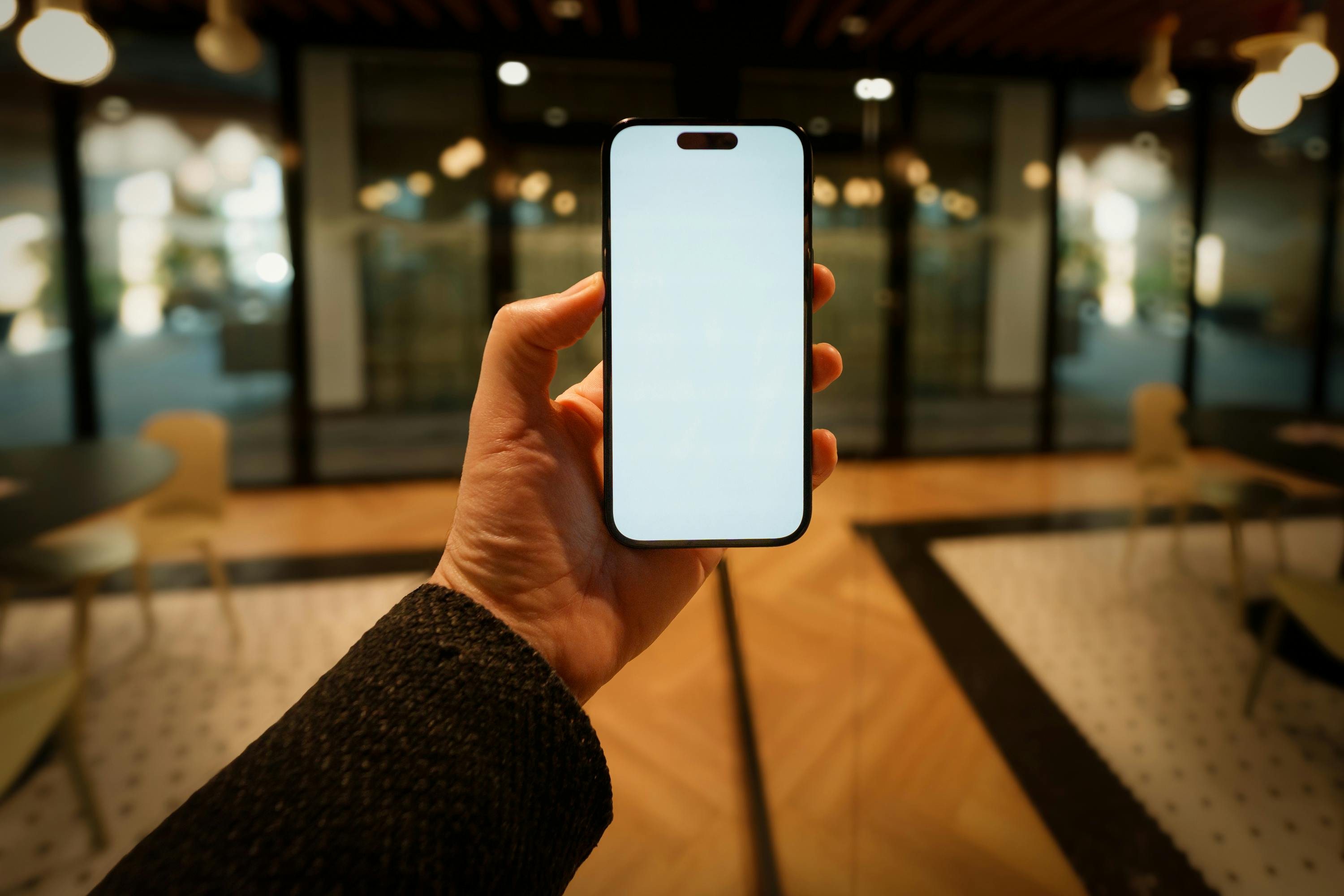 Gratis In un'elegante e moderna hall, una mano regge uno smartphone con lo schermo vuoto, lasciando spazio per eventuali modifiche grafiche. Foto a disposizione