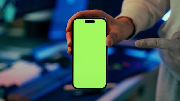 A person holds a smartphone with a green screen in an indoor setting, ideal for mockup designs.