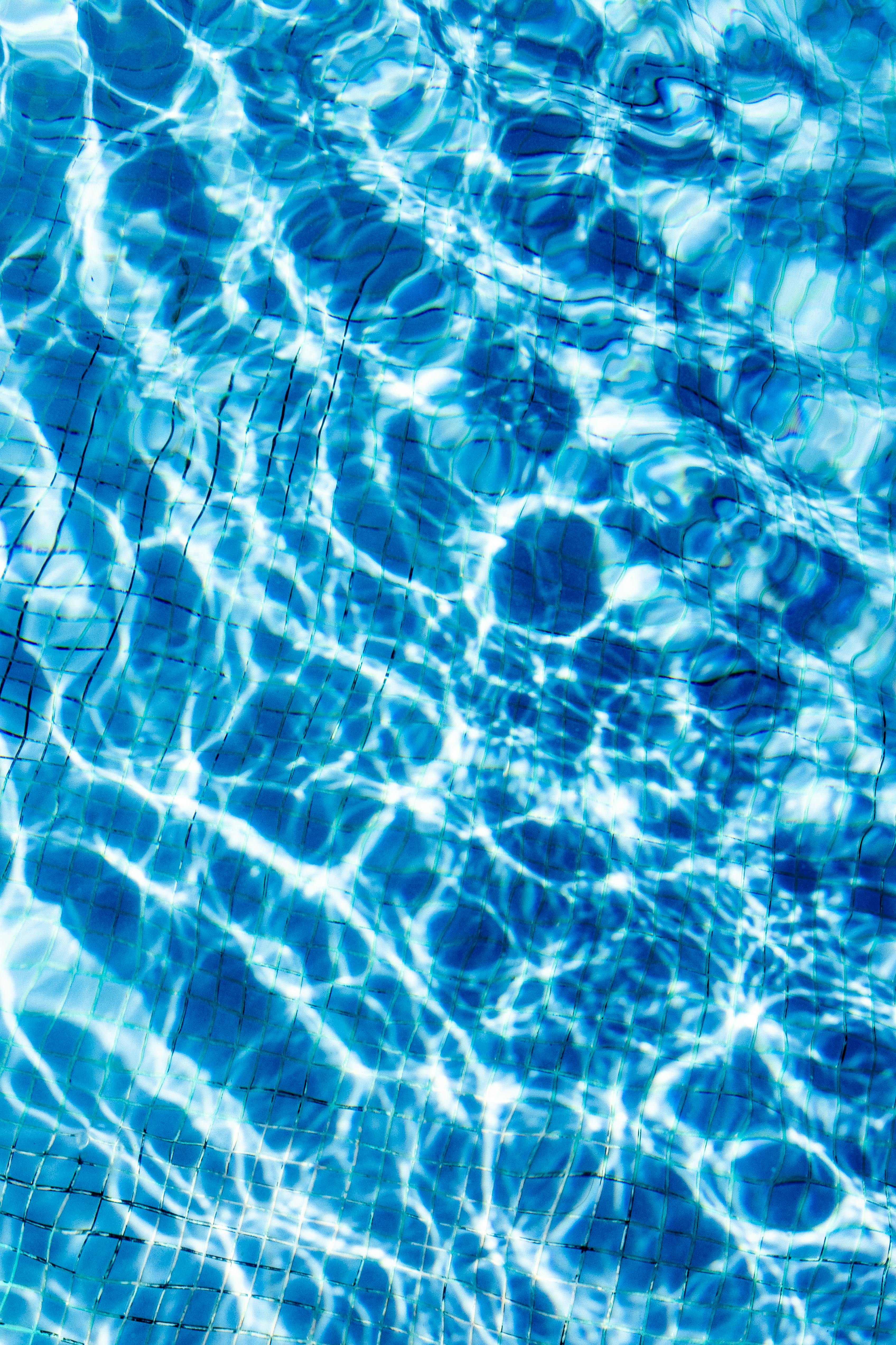 Free Sunlight creates shimmering patterns on a vibrant blue pool surface, capturing the essence of summer relaxation. Stock Photo