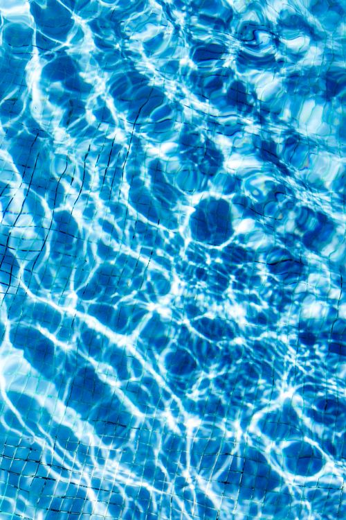 Free Sunlight creates shimmering patterns on a vibrant blue pool surface, capturing the essence of summer relaxation. Stock Photo