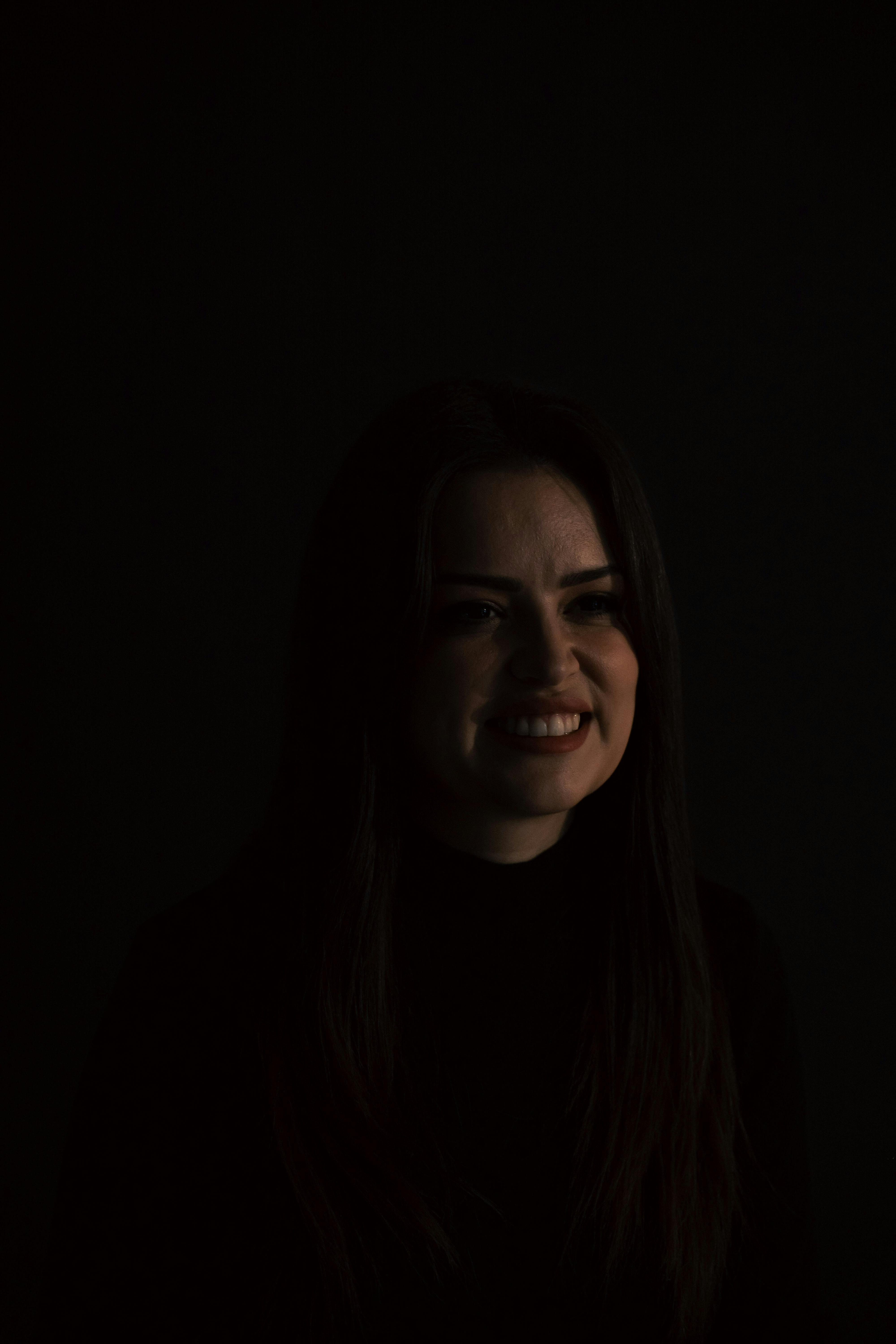 gratis Een ingetogen portret van een vrouw die zachtjes glimlacht in een donkere omgeving, wat een stemmige sfeer creëert. Stockfoto