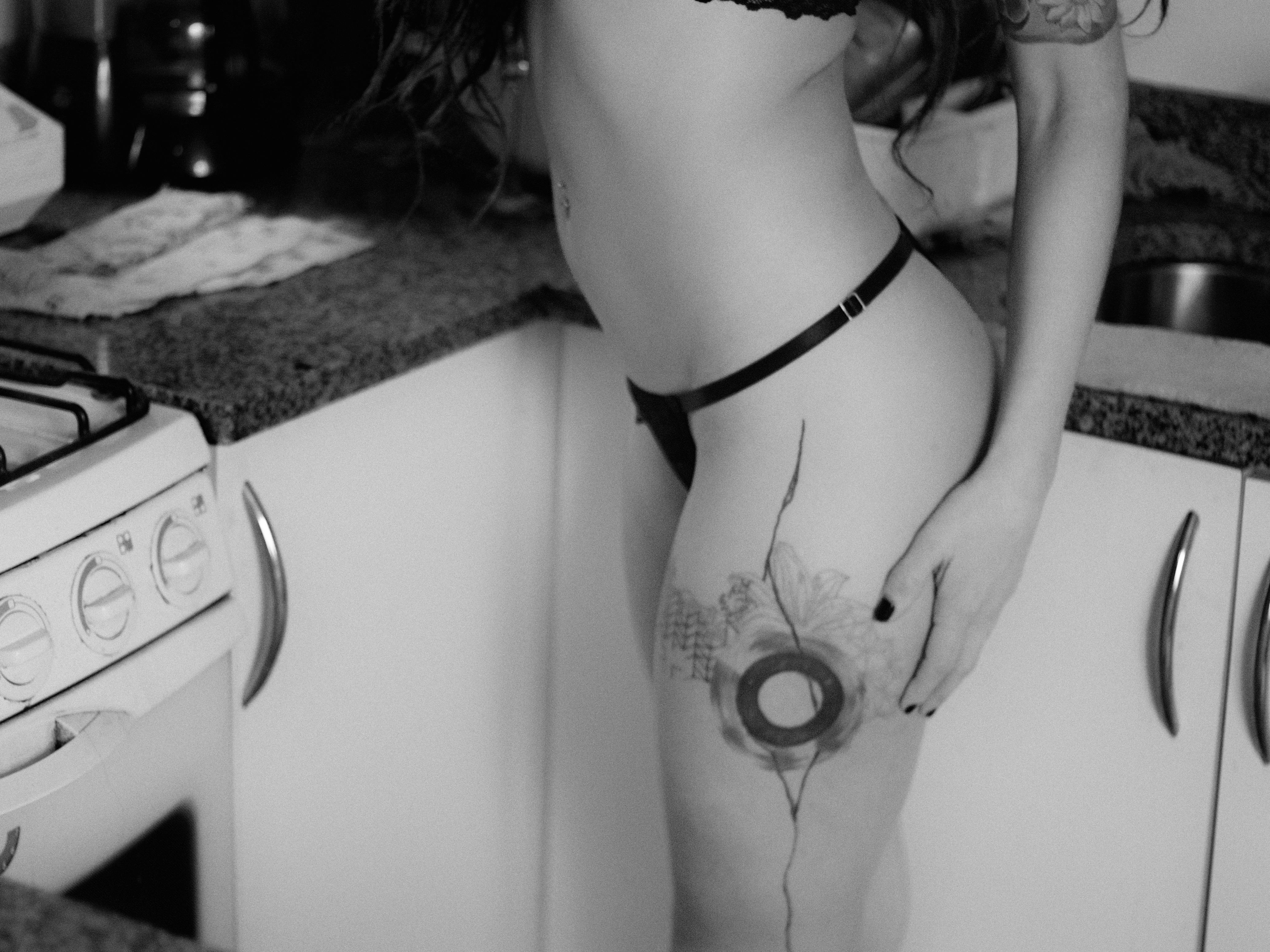 Gratuit Fotografie alb-negru a unei femei cu tatuaj pe coapsă într-o bucătărie. Fotografie de stoc