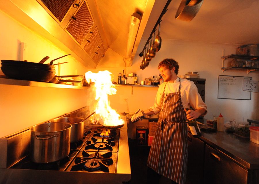 Koch flambiert unter der Abzugshaube einer Restaurantküche