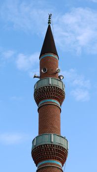Brick minaret with speakers against a blue sky in Konya, Türkiye.