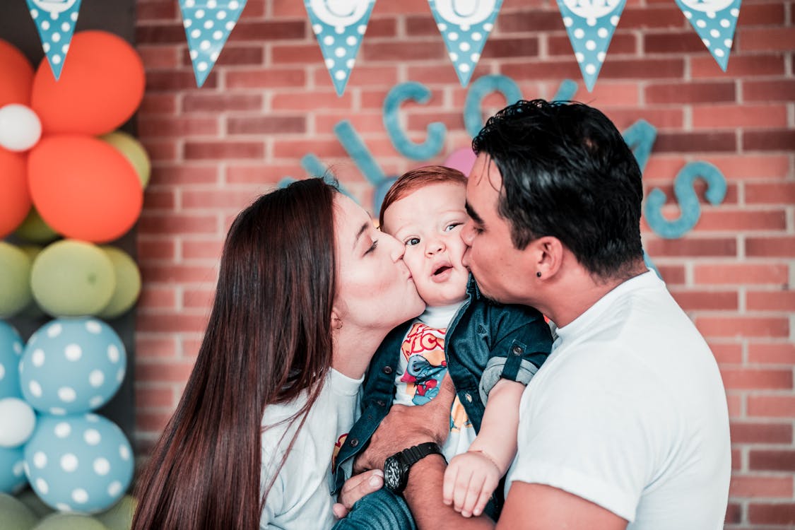 Photo of Man and Woman Kissing Their Baby