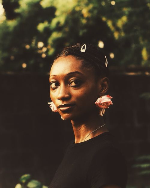 Free A captivating portrait of a woman wearing pink floral earrings outdoors. Stock Photo