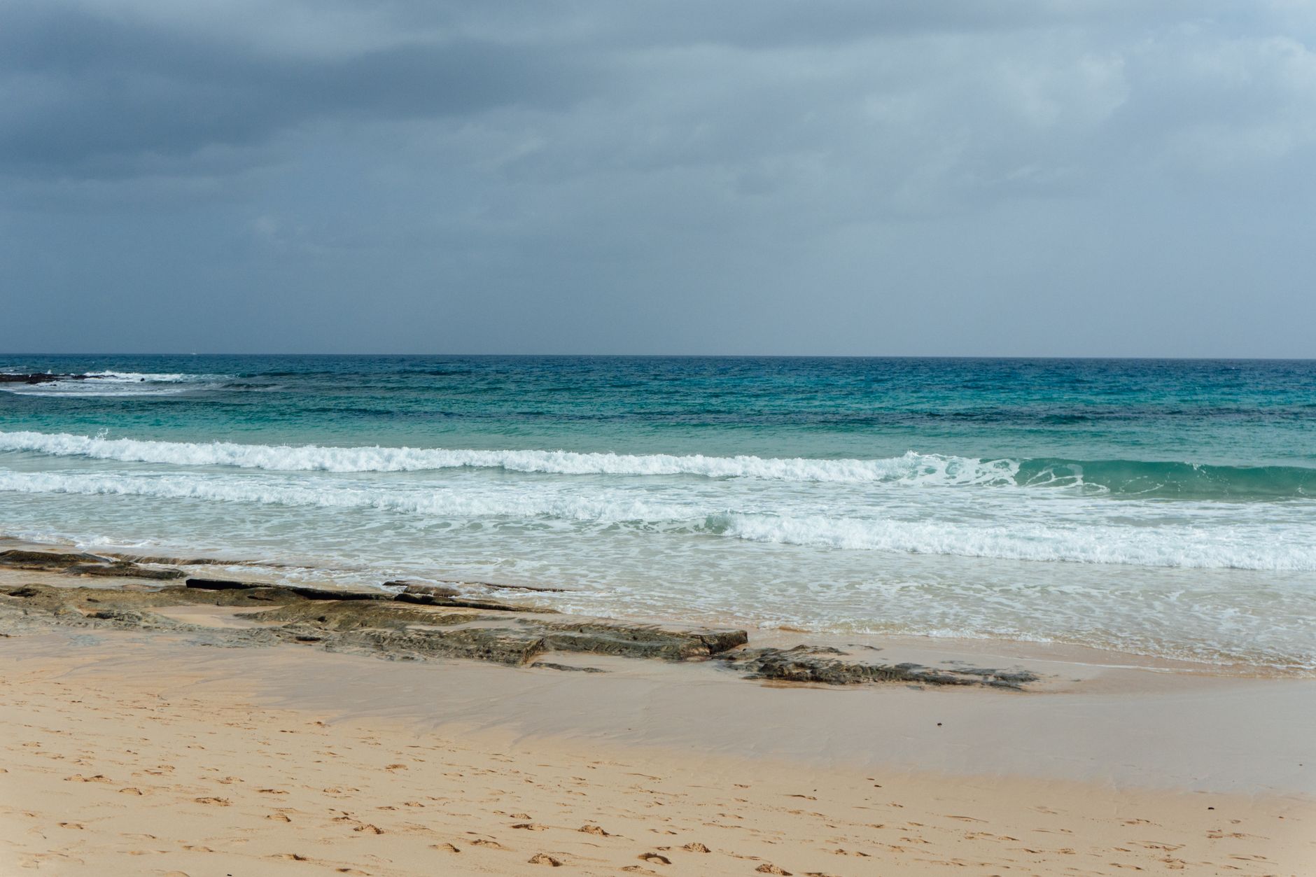 Serene view of a sandy beach and blue ocean waves under a cloudy sky in the Canary Islands.