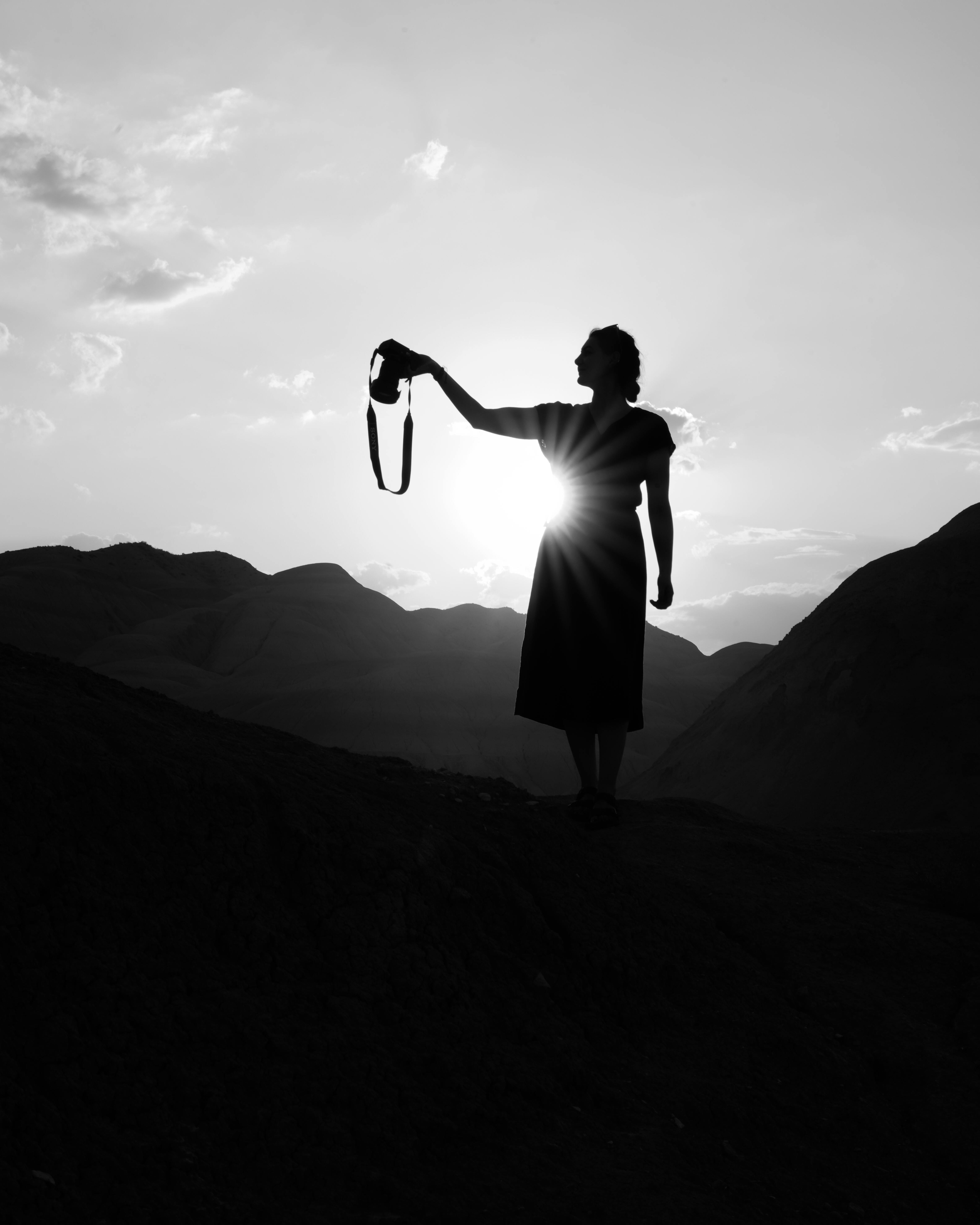 gratis Een dramatisch zwart-wit silhouet van een vrouw met een camera tegen een schilderachtige zonsondergang in de bergen. Stockfoto