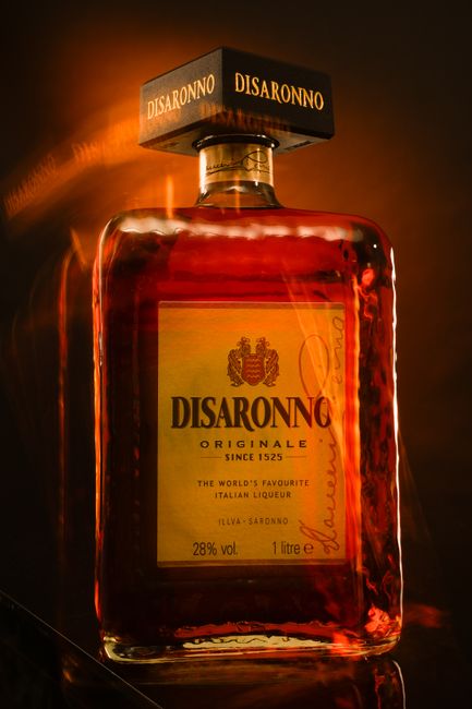 A bottle of amber amaretto liqueur next to a small pour in a glass, surrounded by whole almonds and dried apricot kernels