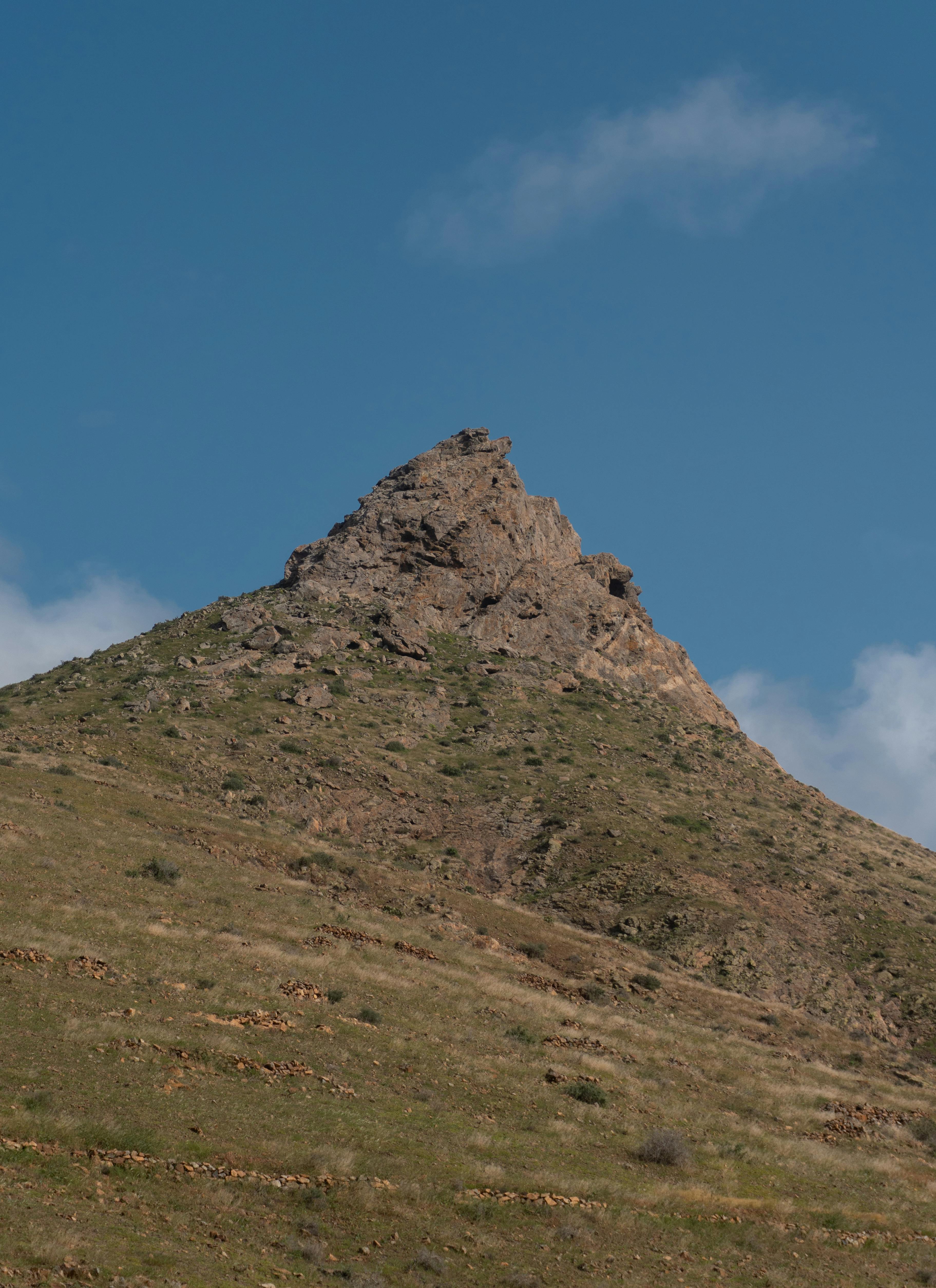 grátis Uma vista panorâmica de um pico rochoso sob um céu azul límpido, exibindo beleza natural e tranquilidade. Foto profissional