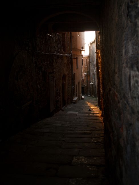 Moody alleyway with stone walls illuminated by warm evening light, creating a mysterious atmosphere.