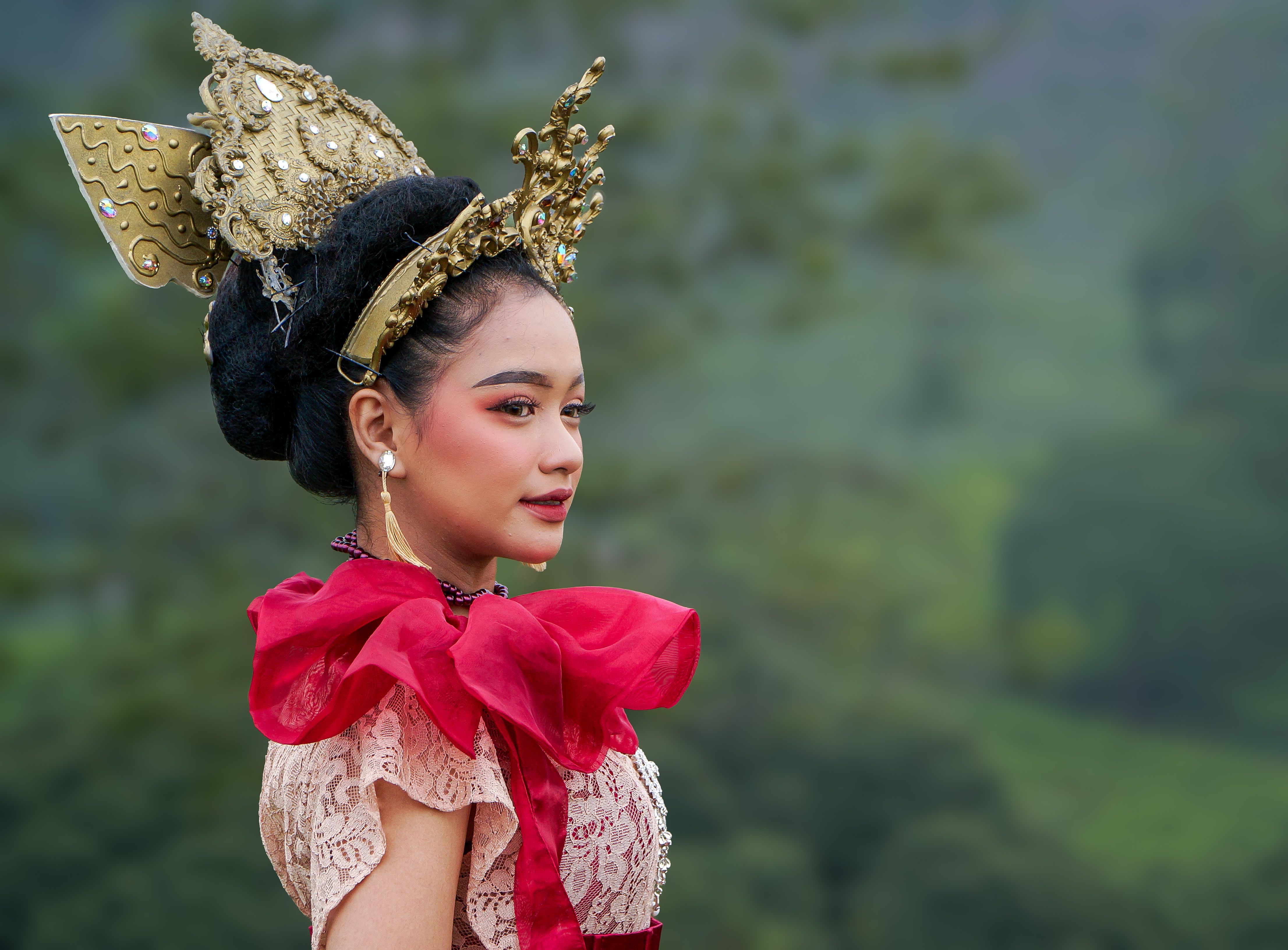 Mulher vestida com traje tradicional, usando adereços elaborados e uma coroa decorada, em meio à paisagem natural, representando a cultura e as tradições locais.