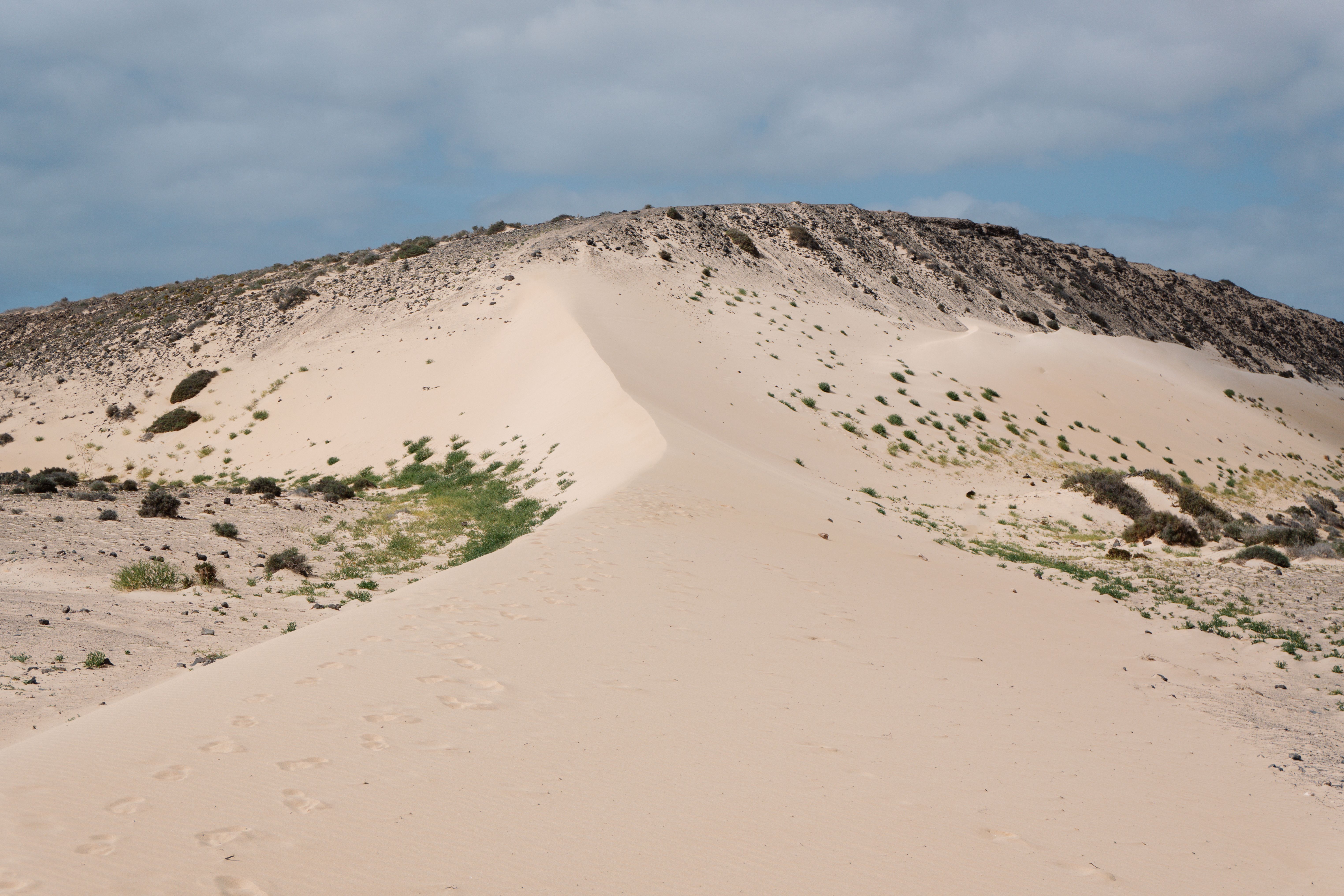 Expansive sand dune with sparse vegetation under a partly cloudy sky.