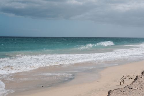 Free Calm ocean waves gently crash on a sandy beach under a cloudy sky, ideal for relaxation themes. Stock Photo