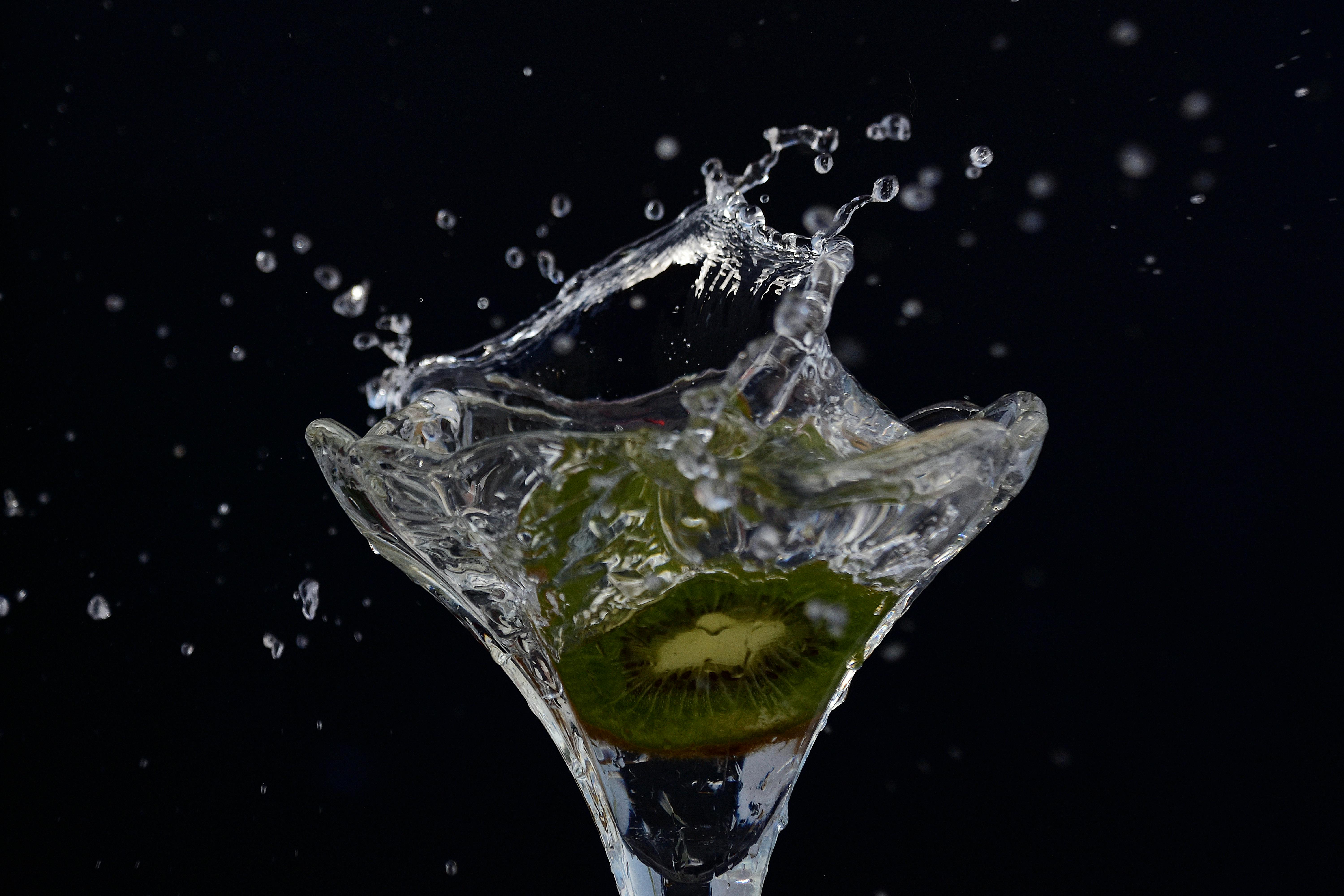 Ücretsiz Koyu bir arka plan önünde, martini kadehinin içinde su altında çırpınan bir kivi meyvesinin yakın çekim görüntüsü. Stok Fotoğraflar