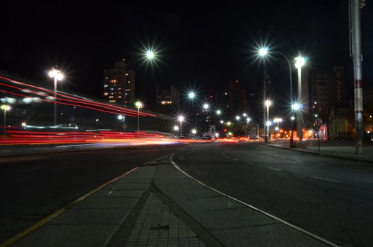 City street at night with vibrant light trails from passing cars, capturing urban energy.