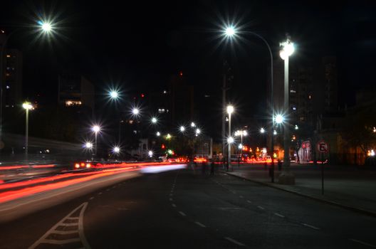 City street at night with long exposure light trails and illuminated street lamps.